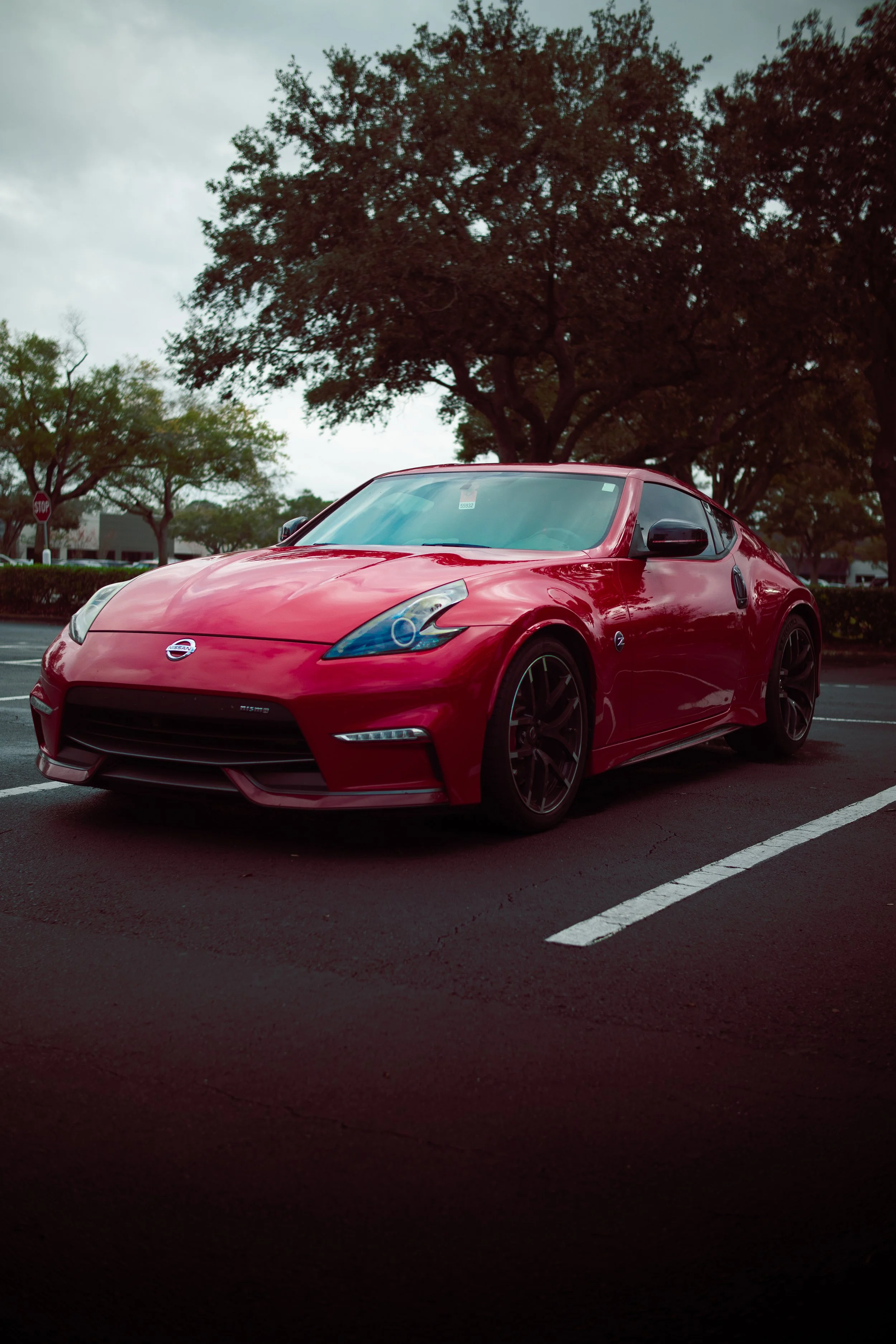 Red sports car parked in a parking lot with trees and overcast sky in the background.