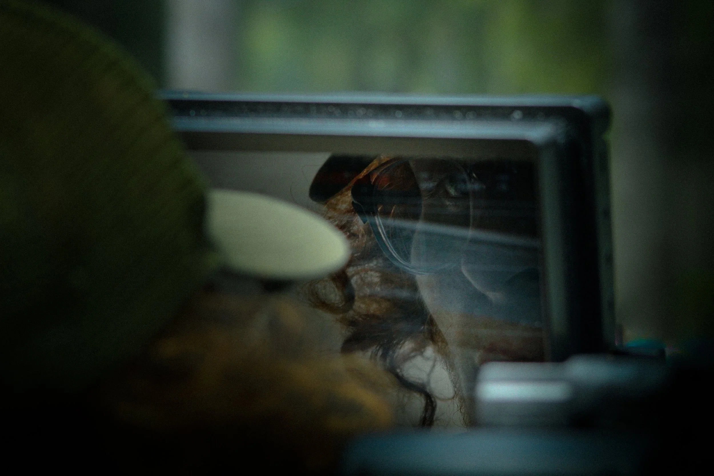 A blurry image taken through a glass surface shows a refrigerator with a wig inside, surrounded by various objects.