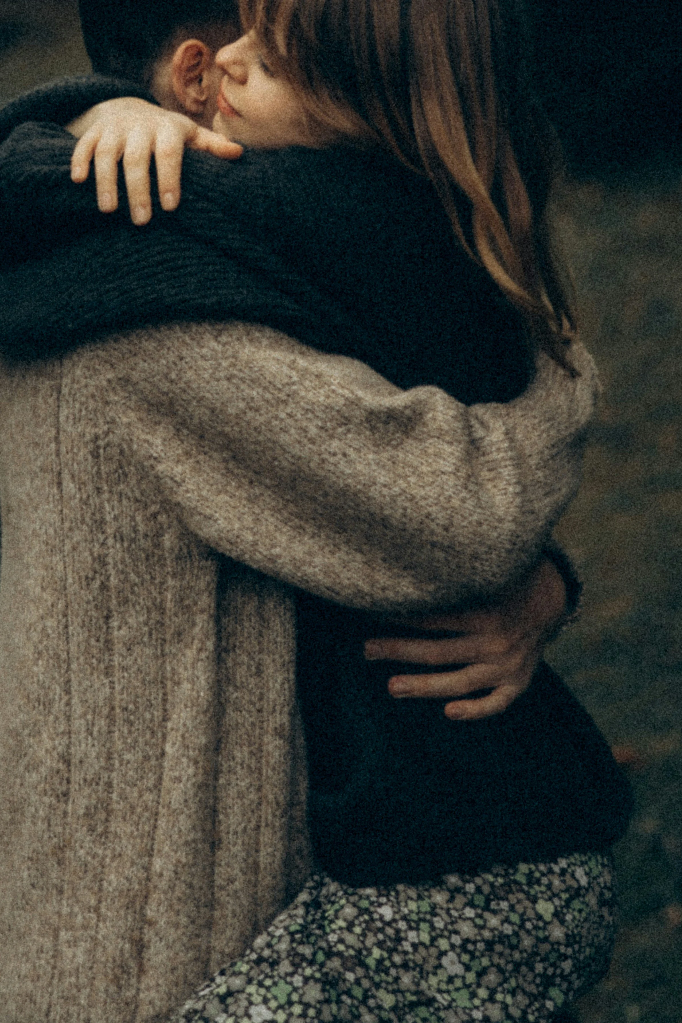 A woman with red hair hugging a person with short dark hair, their faces close together, in a warm embrace.
