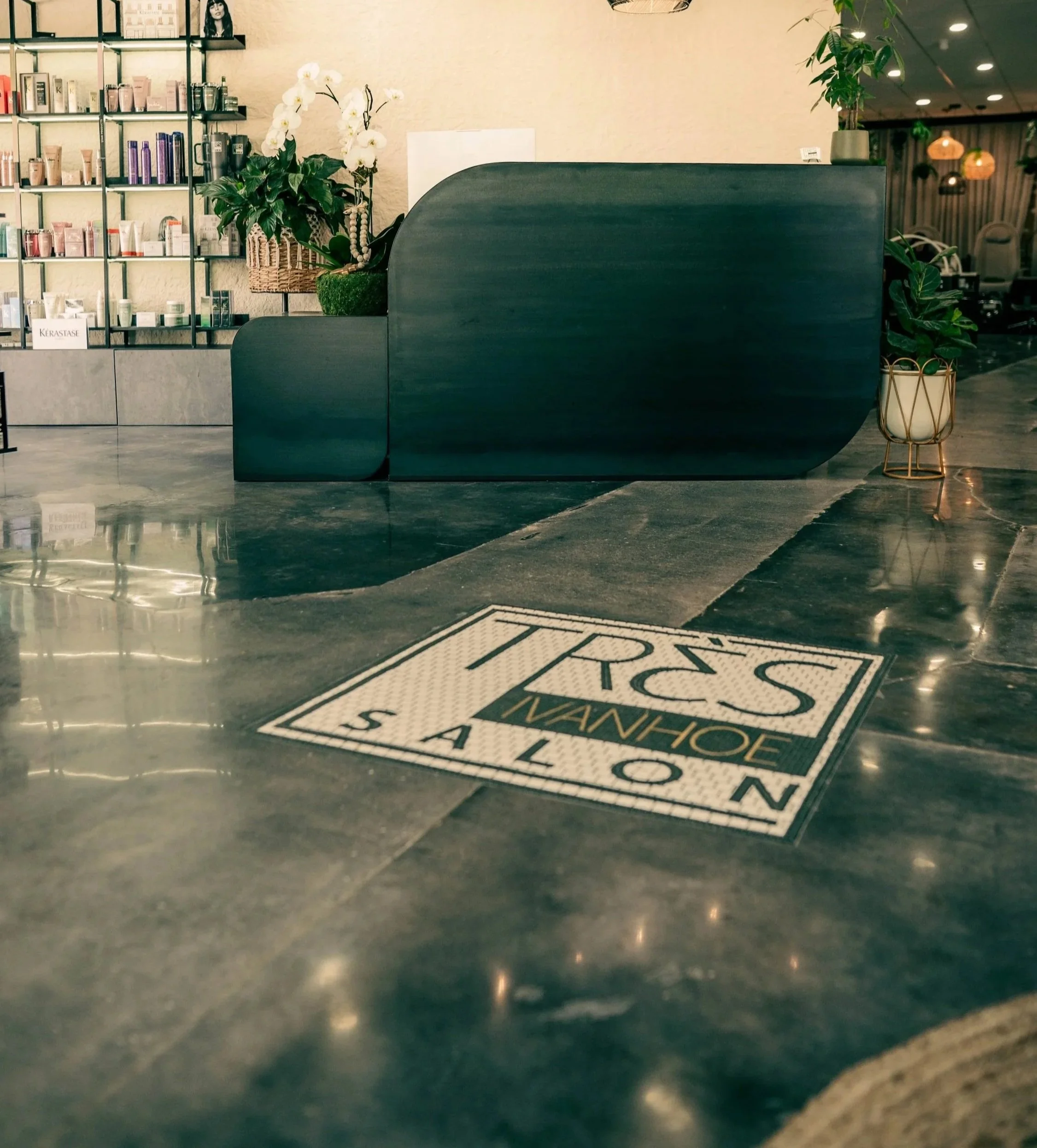 The Très Ivanhoe Salon logo displayed on the polished concrete floor of our modern luxury salon in Orlando, welcoming guests to a complete self-care escape.