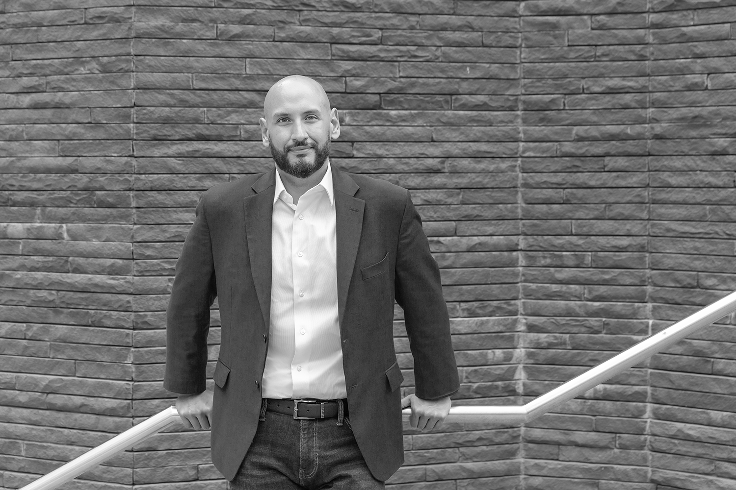 Marcos Torres, leadership advisor and keynote speaker, standing next to a metal railing in front of a brick wall.