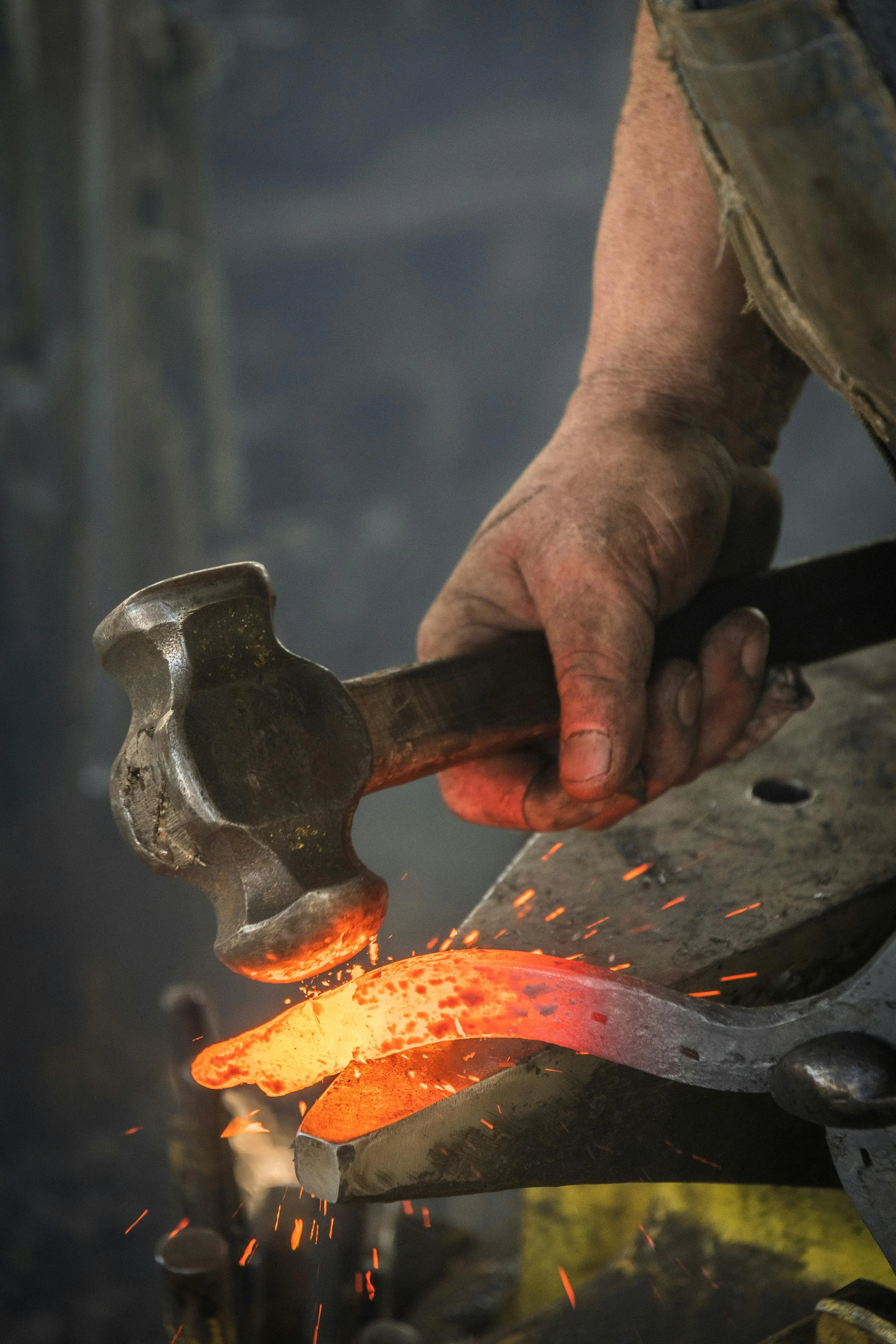 A blacksmith shaping hot metal with a hammer in a forge, sparks flying.