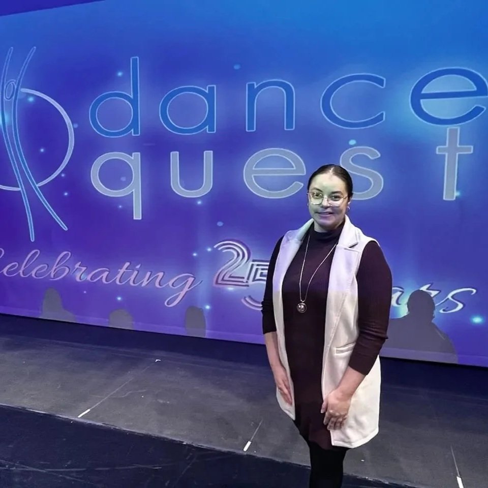 A woman standing in front of a large screen that reads 'dance quest celebrating 25 years'.