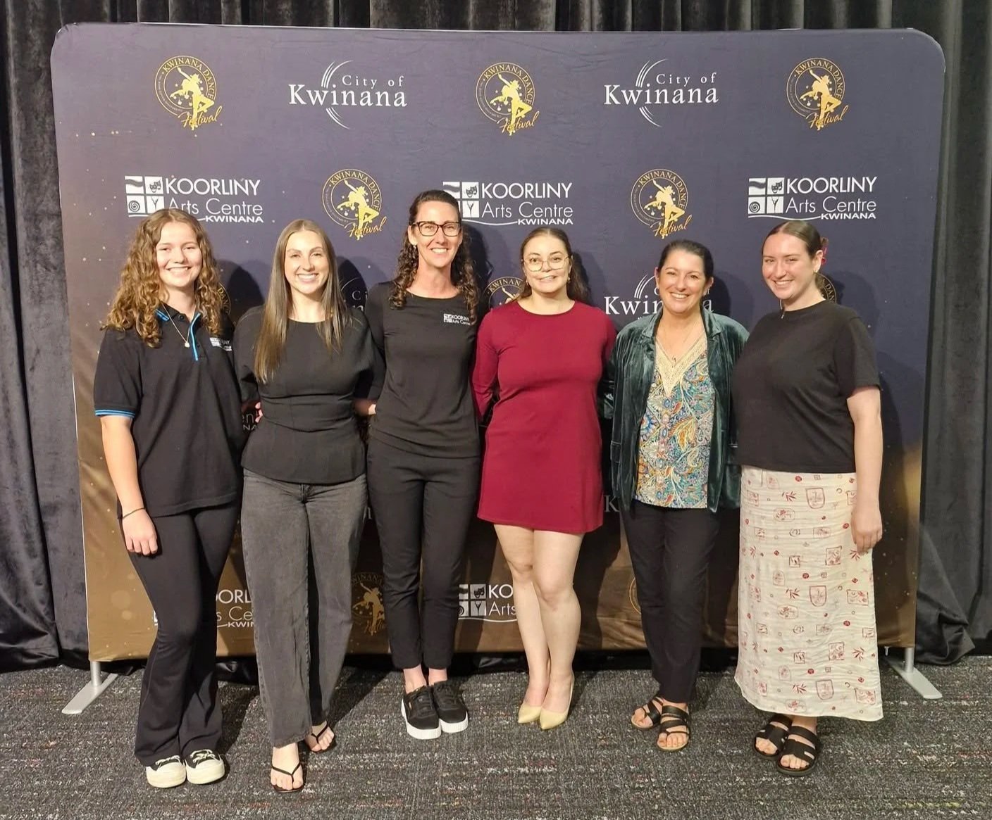 Group of six women standing in front of a backdrop with logos for the City of Kwinana and Koorliny Arts Centre, smiling and posing for the photo.