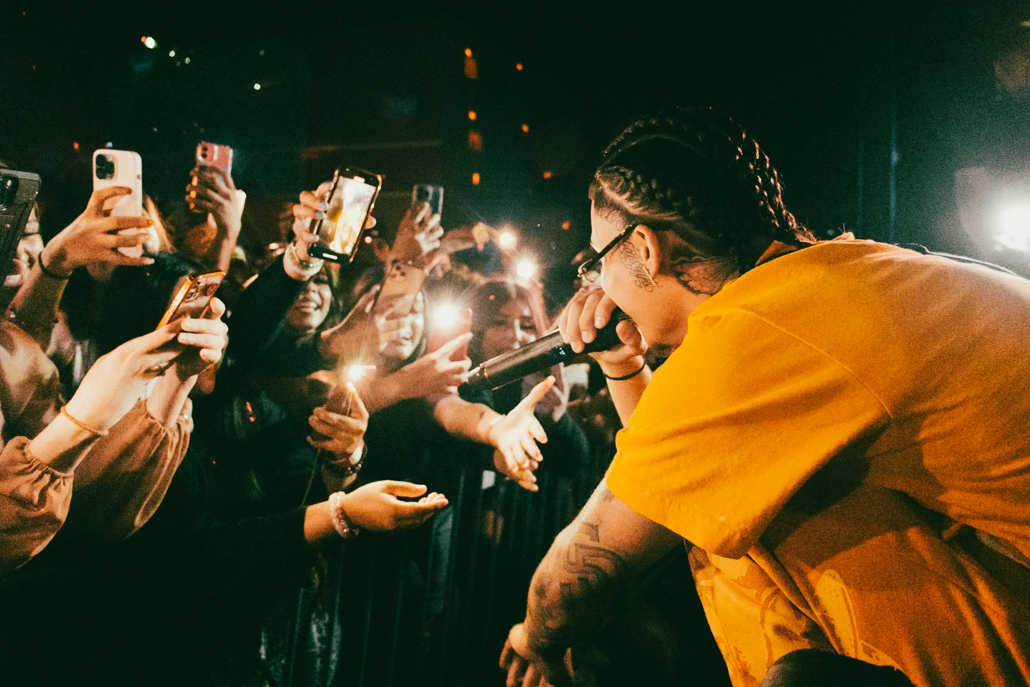 Musician performing on stage in front of a crowd holding up their phones to take pictures.