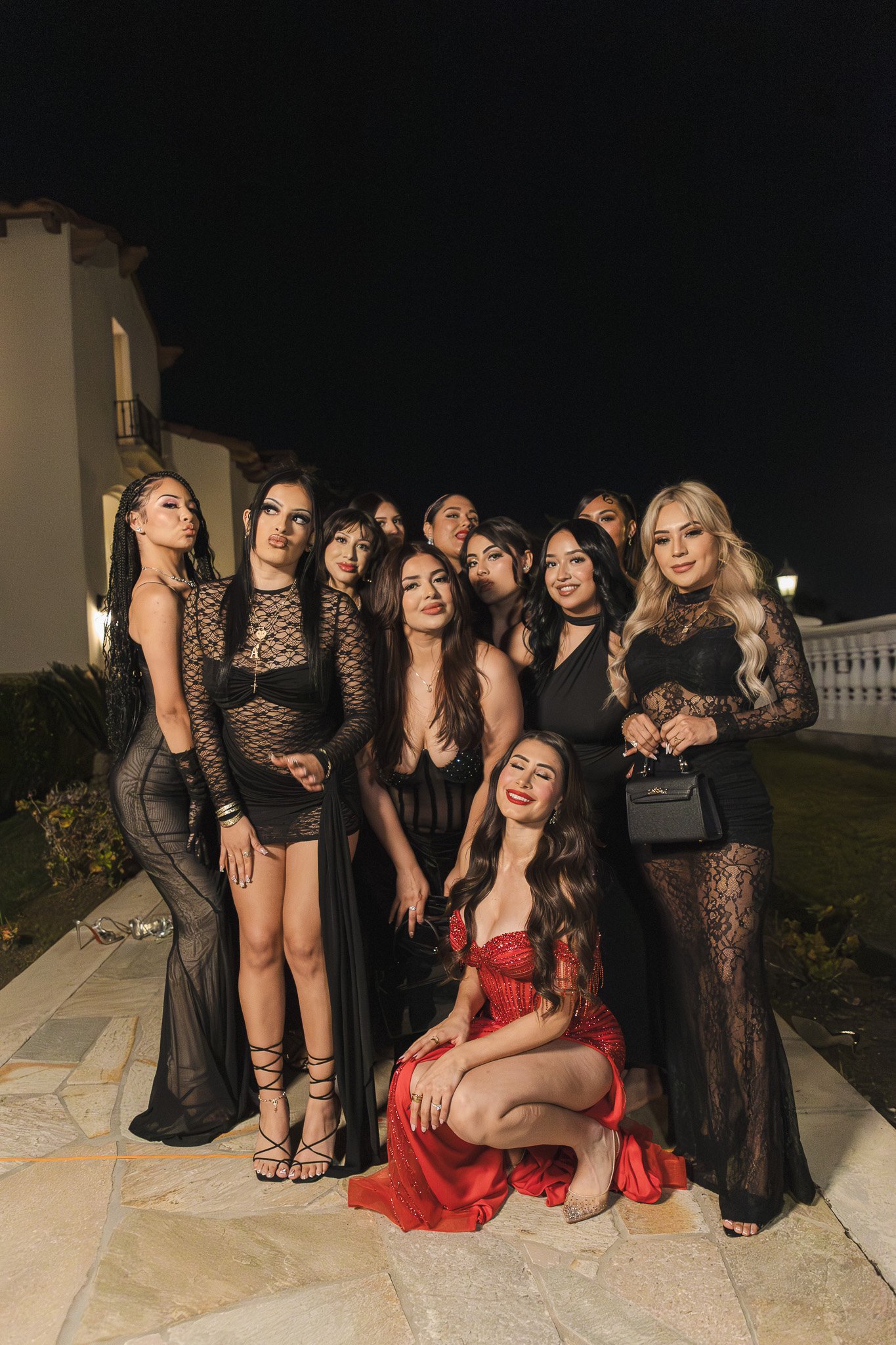 Group of women dressed in black and red evening gowns at night, posing outdoors.
