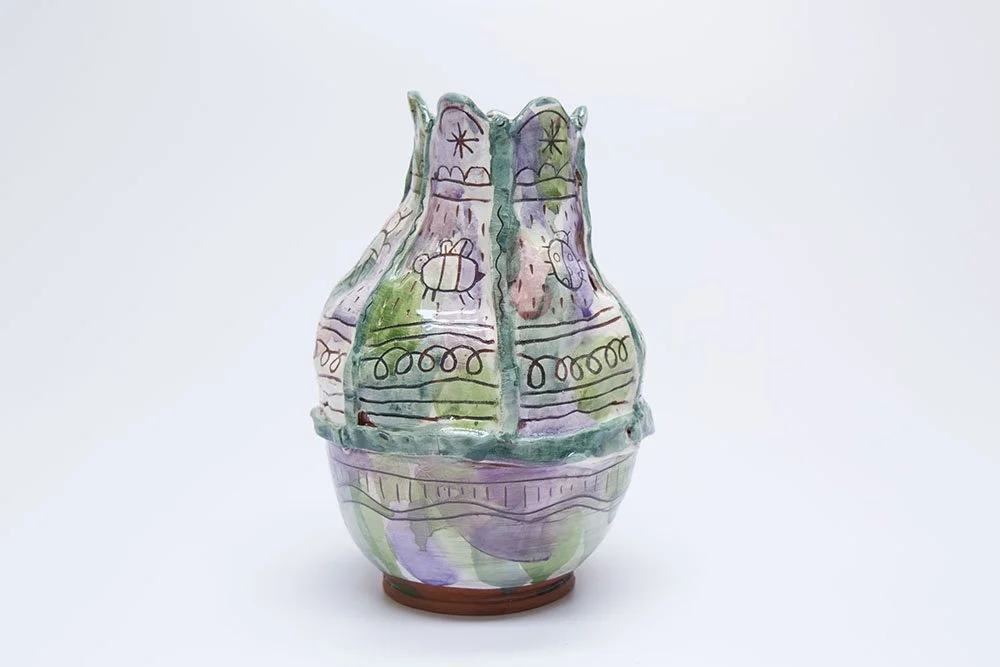 Colorful ceramic vase with abstract, whimsical designs in purple, green, and pink, set against a plain white background.