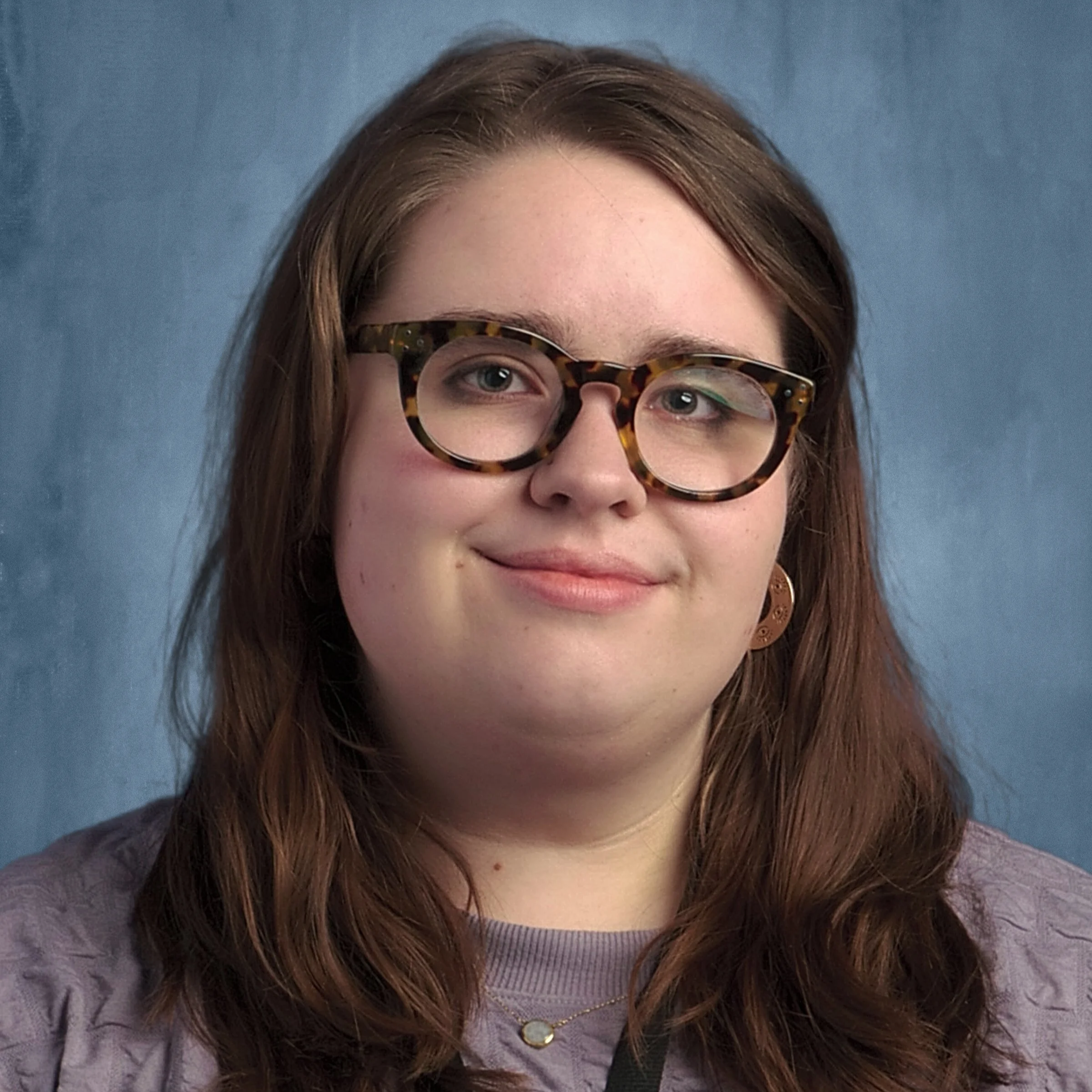 A woman with brown hair and glasses with a tortoiseshell pattern, smiling against a blue background.