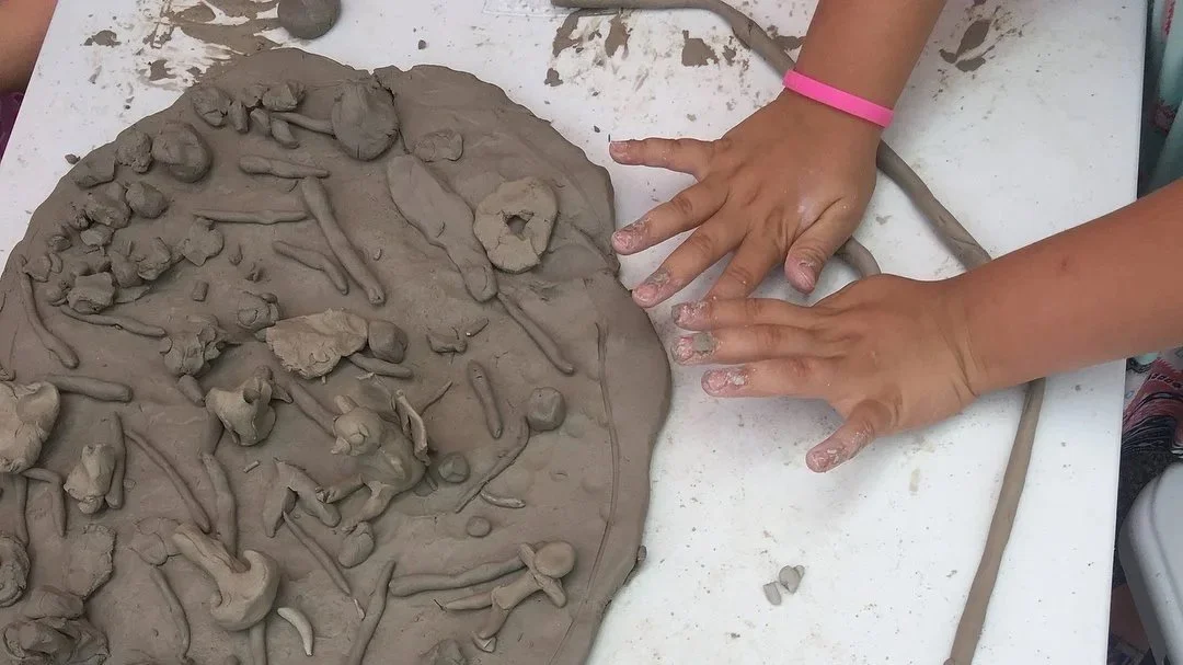 Child's hands shaping and pressing clay with other small sculptures on it.