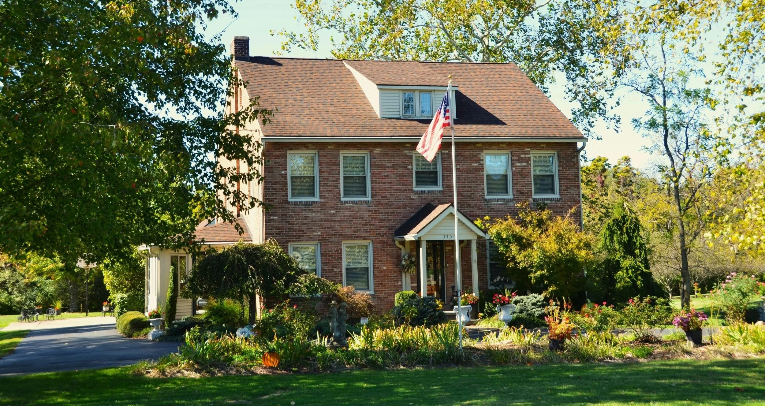 A tradition brick two-story home with an American flagpole out front, with a lush green garden filling the front lawn.