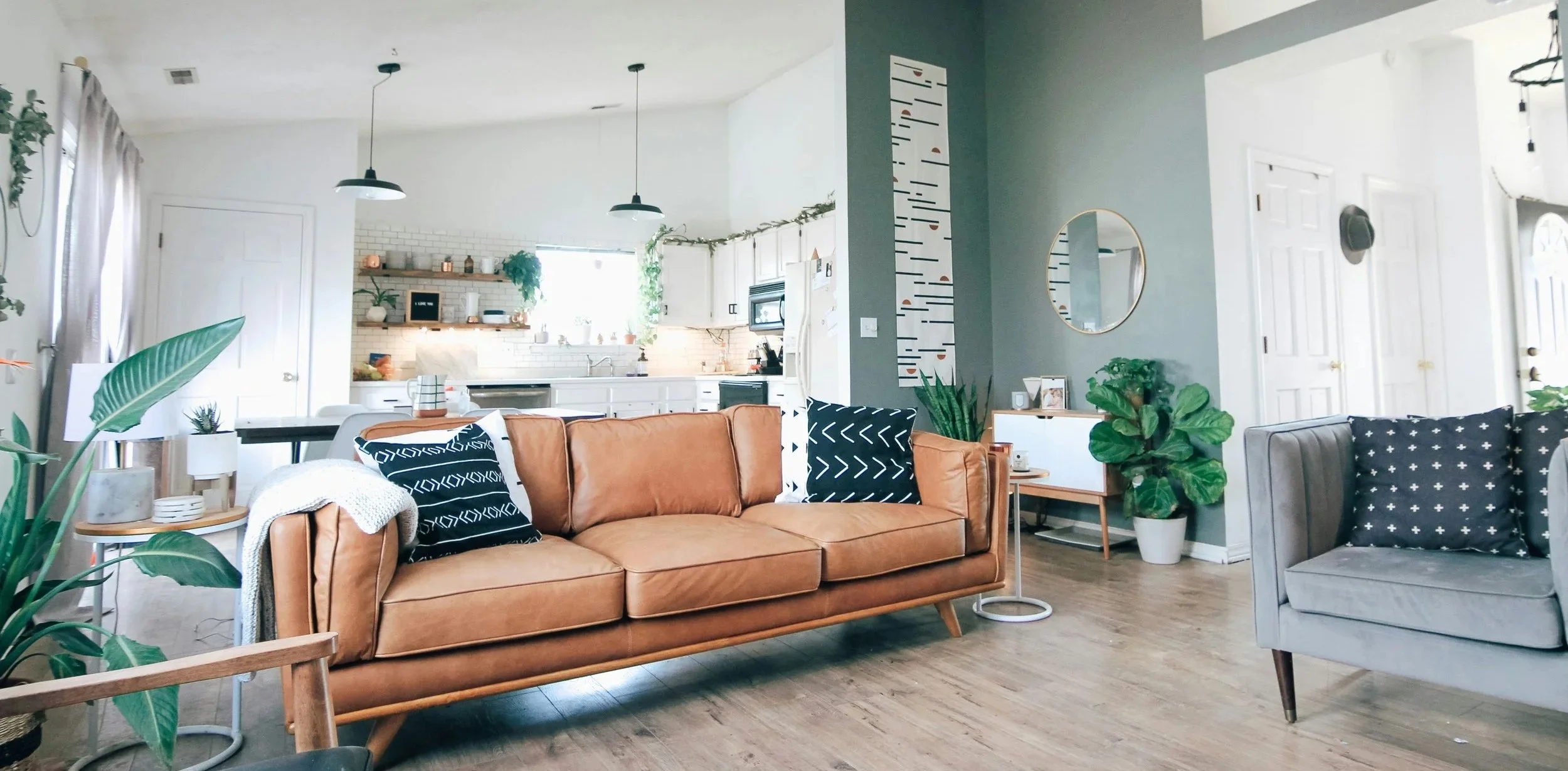 A well lit, modern living room with a leather couch and a modern white kitchen in the background