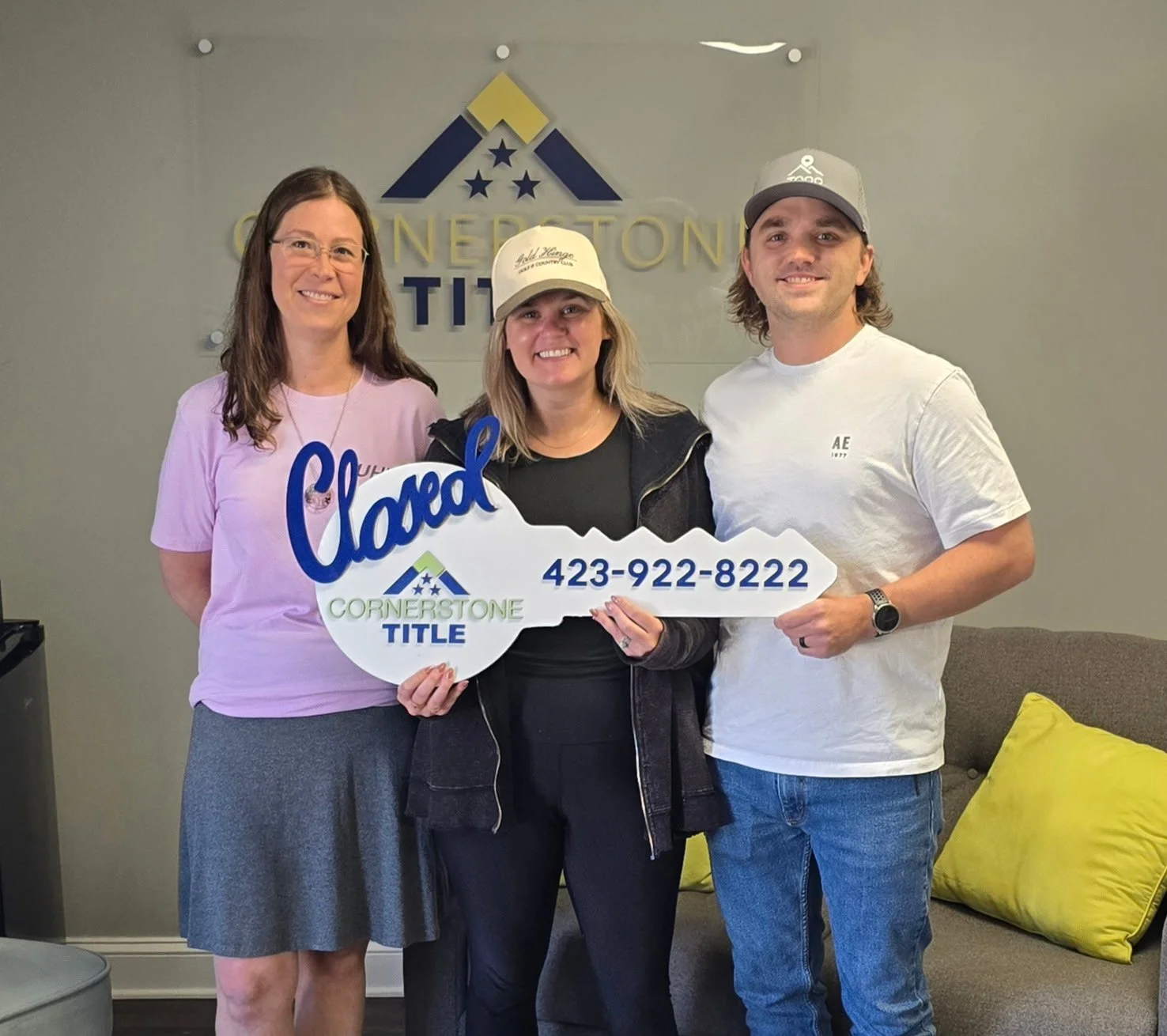 Two happy new homeowners and Katherine holding a "Closed" sign marking their home purchase
