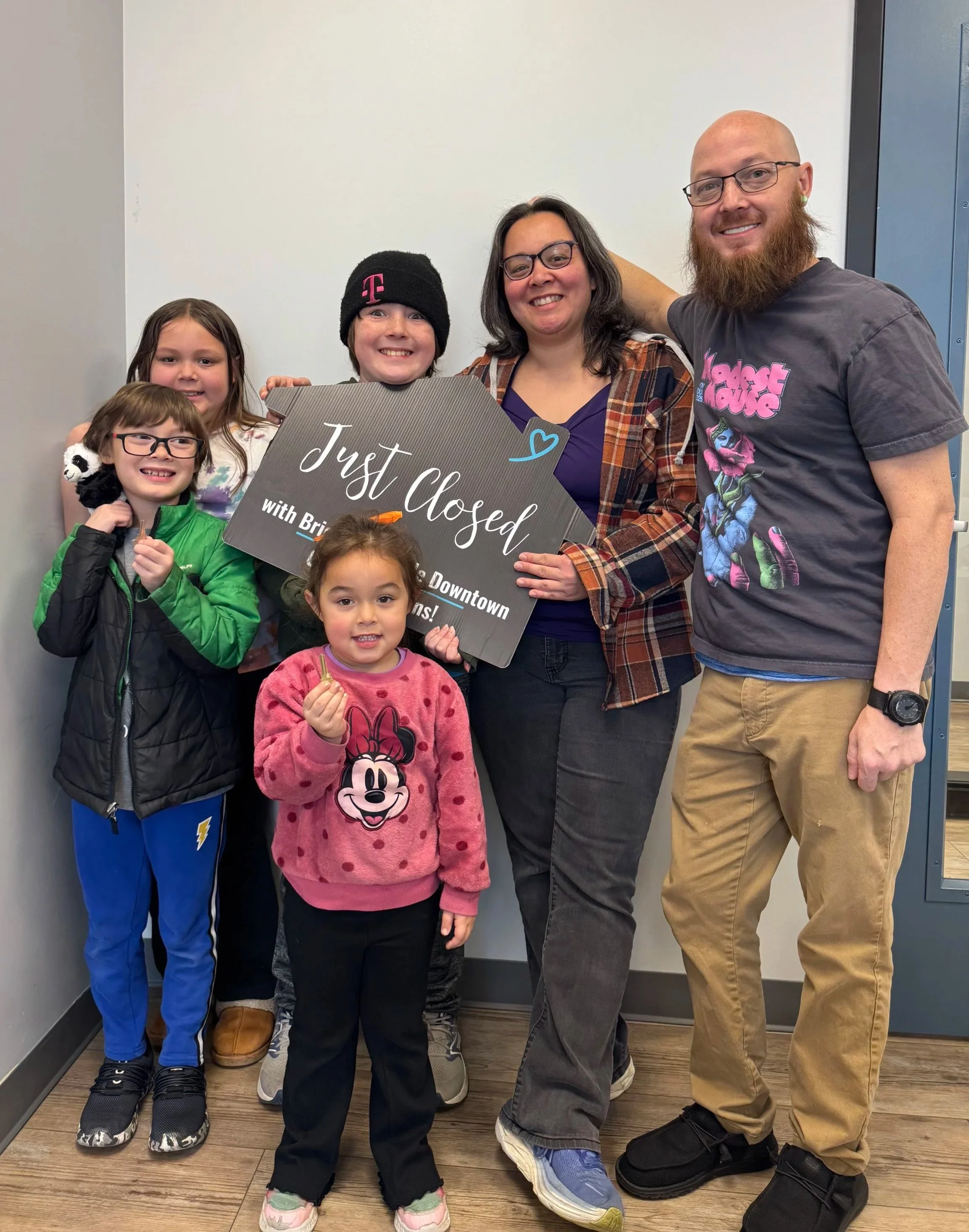 A happy family of six holding their "Just Closed" sign to celebrate their home purchase