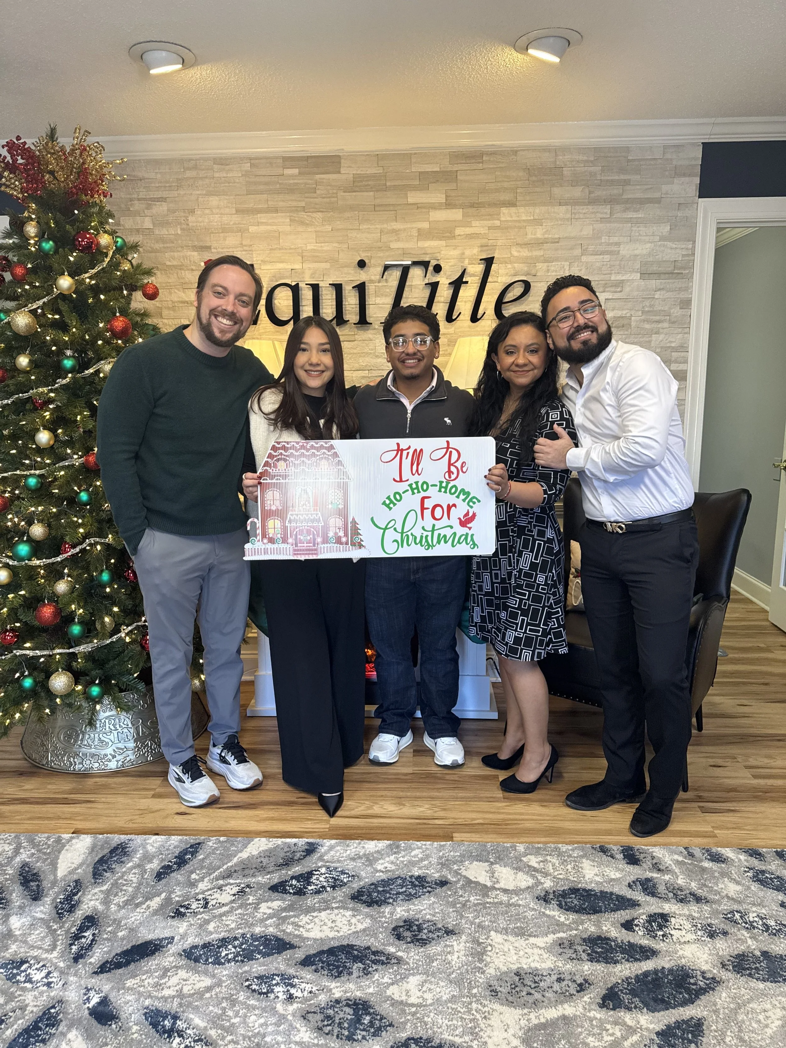 Corey and a family of four happily holding a "I'll be Ho-ho-home for the Holidays" sign to celebrate their home purchase in time for the winter holidays