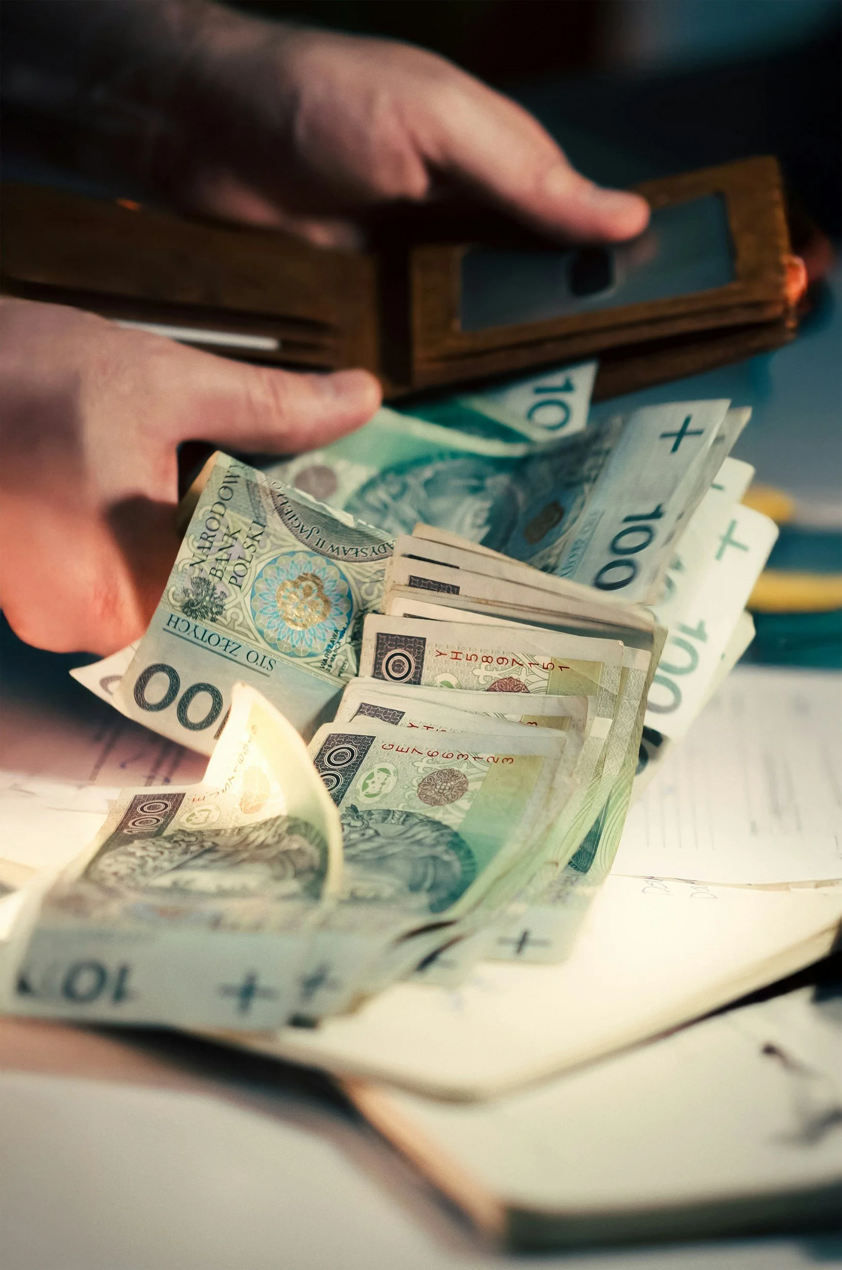 Hands holding a wallet with scattered cash on a table around an open notebook.