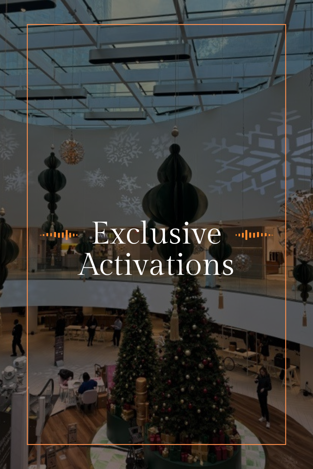 Christmas trees decorated with ornaments and presents underneath, holiday decorations including paper lanterns and snowflake projections inside a modern shopping mall.