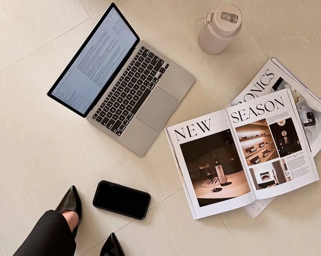 A laptop, a smartphone, a water bottle, a magazine, and a pair of shoes on a light-colored tiled floor.