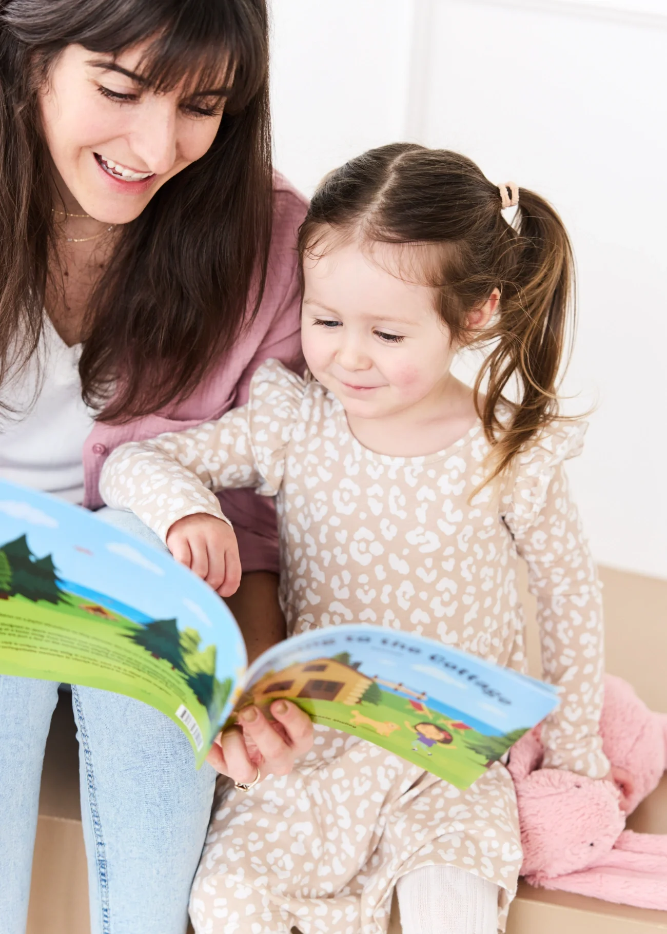 Cassie Shelley and her daughter reading her book together. Her daughter is pointing to a page in the book.