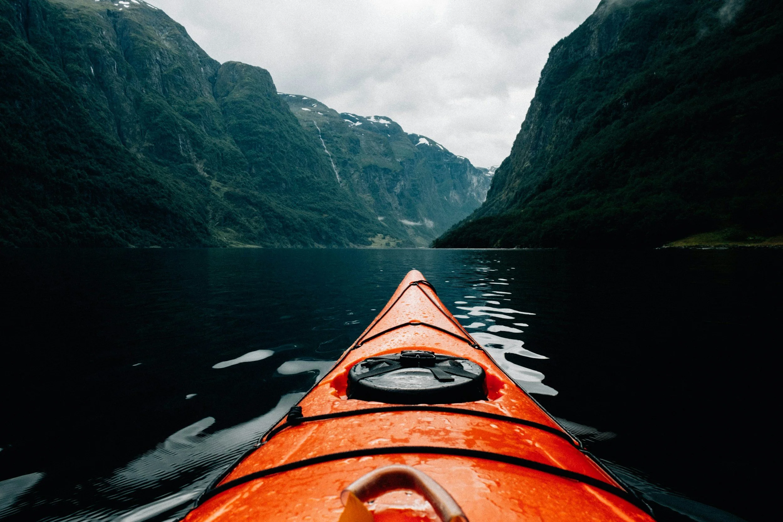 View from a kayak in a fjord, with steep, green mountains on either side and overcast sky.
