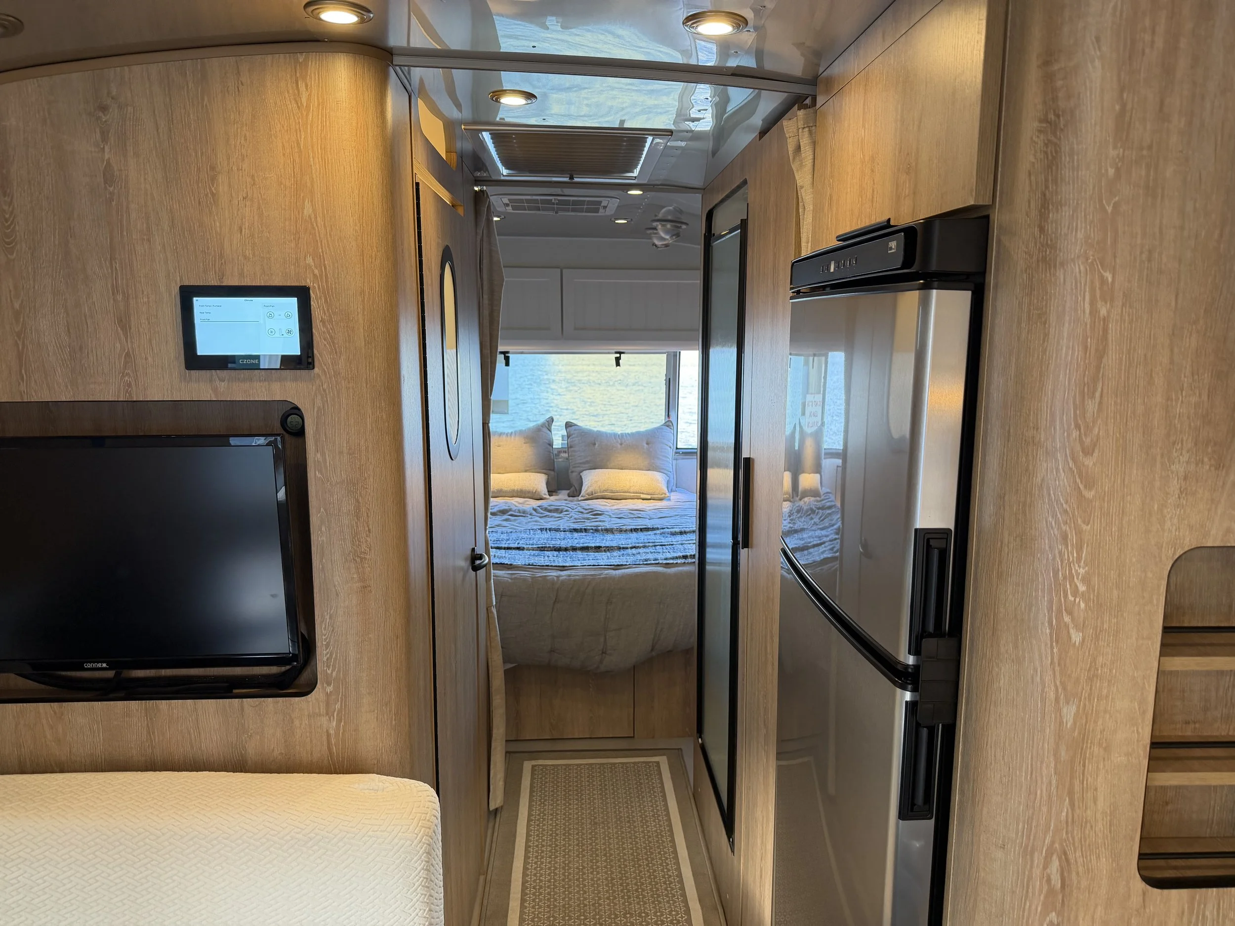 Interior of a yacht or boat with a small kitchen area, a bed with pillows, a small television on the wall, and a window overlooking water.