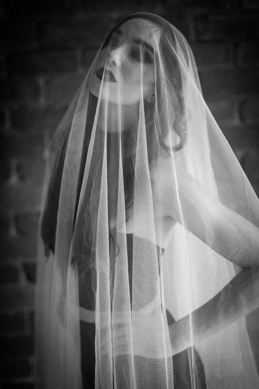 A woman wearing a veil posed in front of a brick wall, with her hand on her hip.