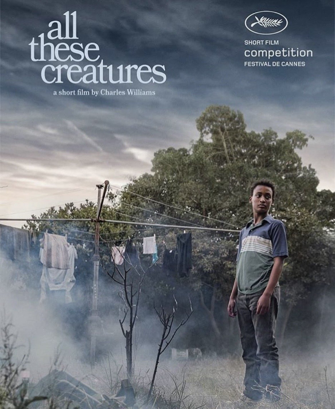 Poster for short film titled 'All These Creatures' by Charles Williams. Features a young boy standing outdoors near a clothesline with laundry hanging, smoke in the foreground, and a cloudy sky in the background. Includes Cannes Film Festival logo an