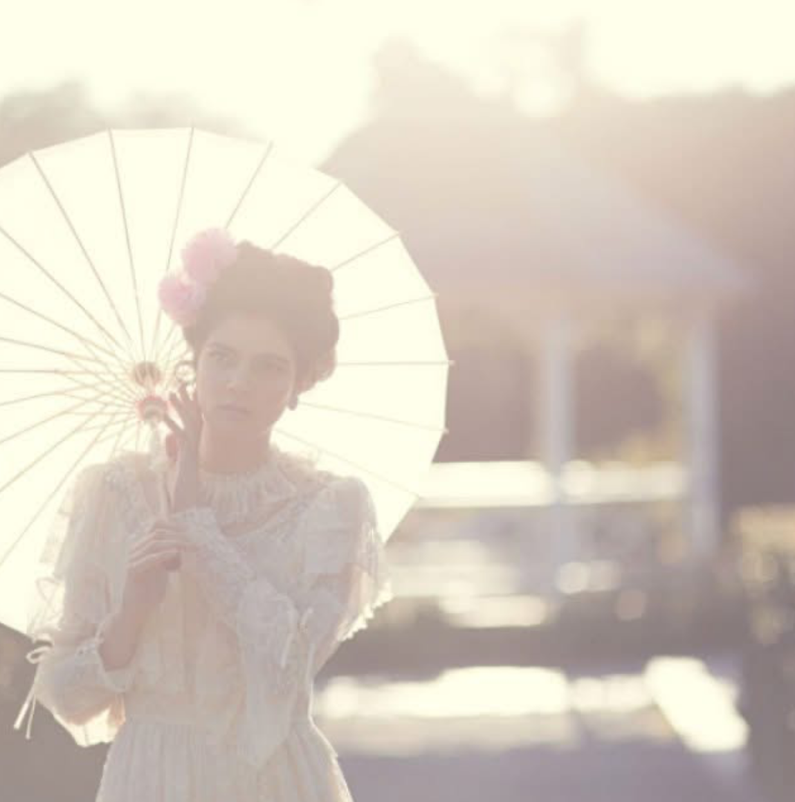 A woman in a lace dress holding a parasol in bright sunlight, with a blurred outdoor background.