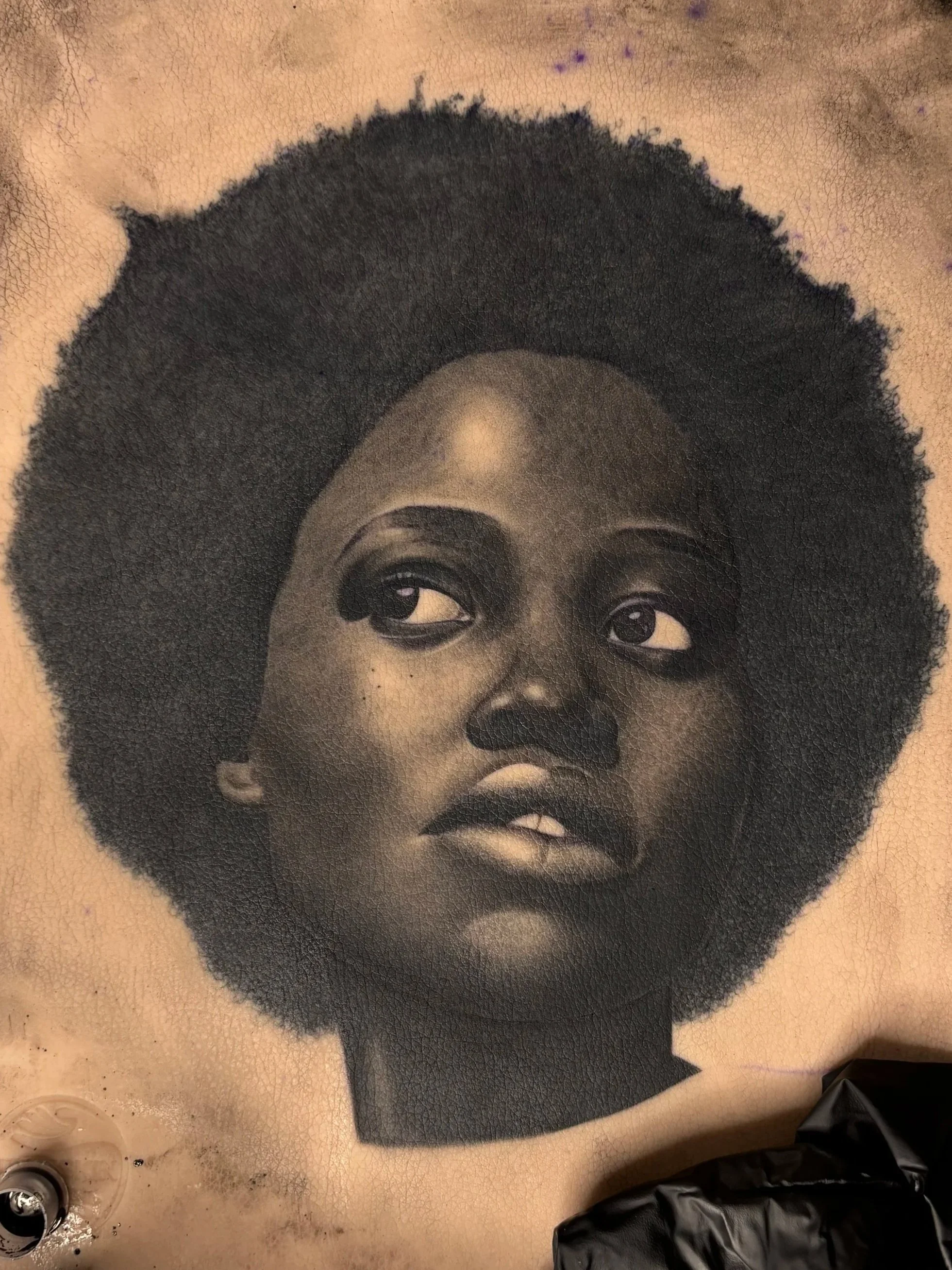 Close-up of a tattoo of a young black woman's face with an afro hairstyle on a person's skin.