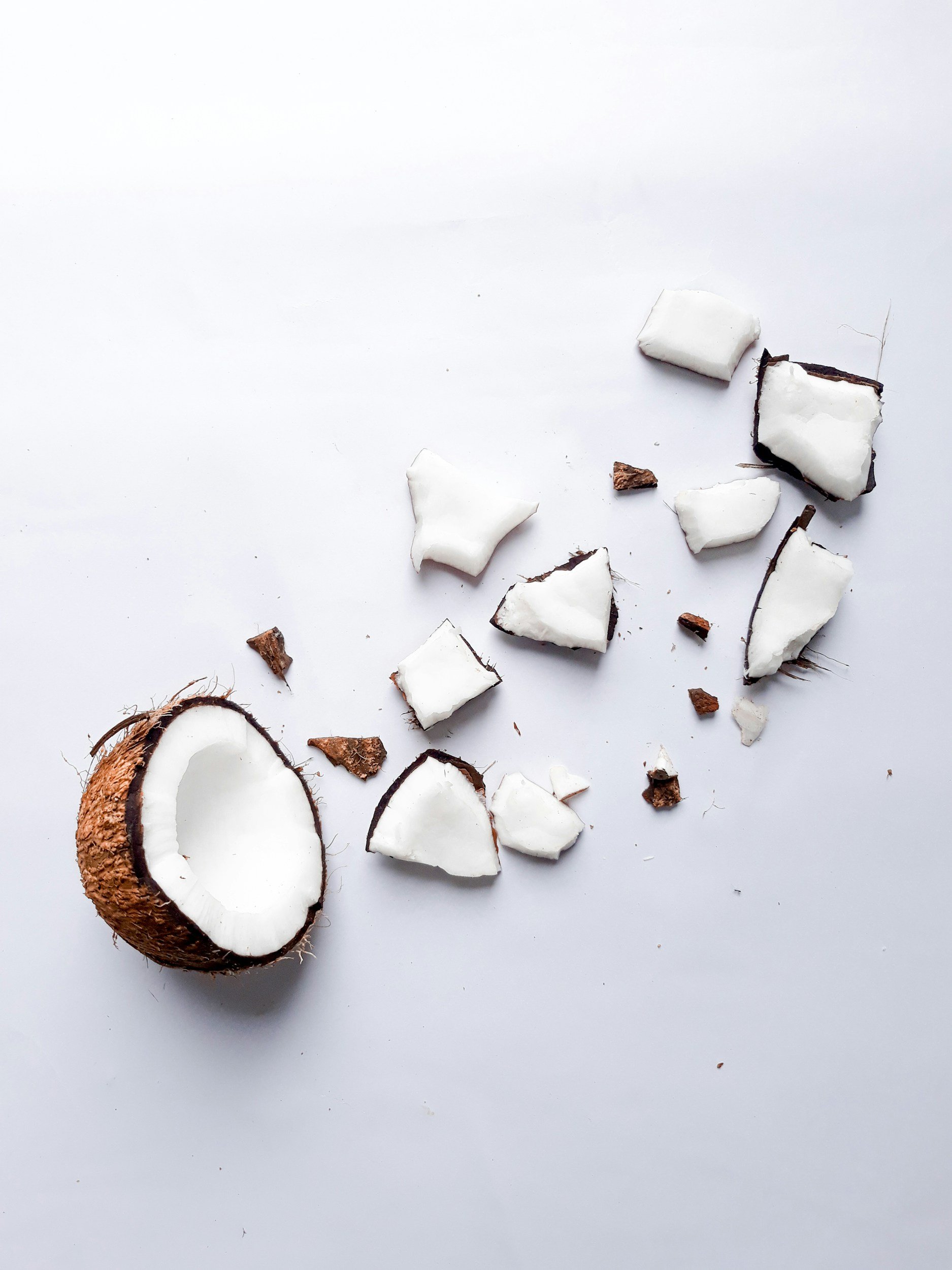 Broken coconut with pieces and crumbs scattered on a white surface.