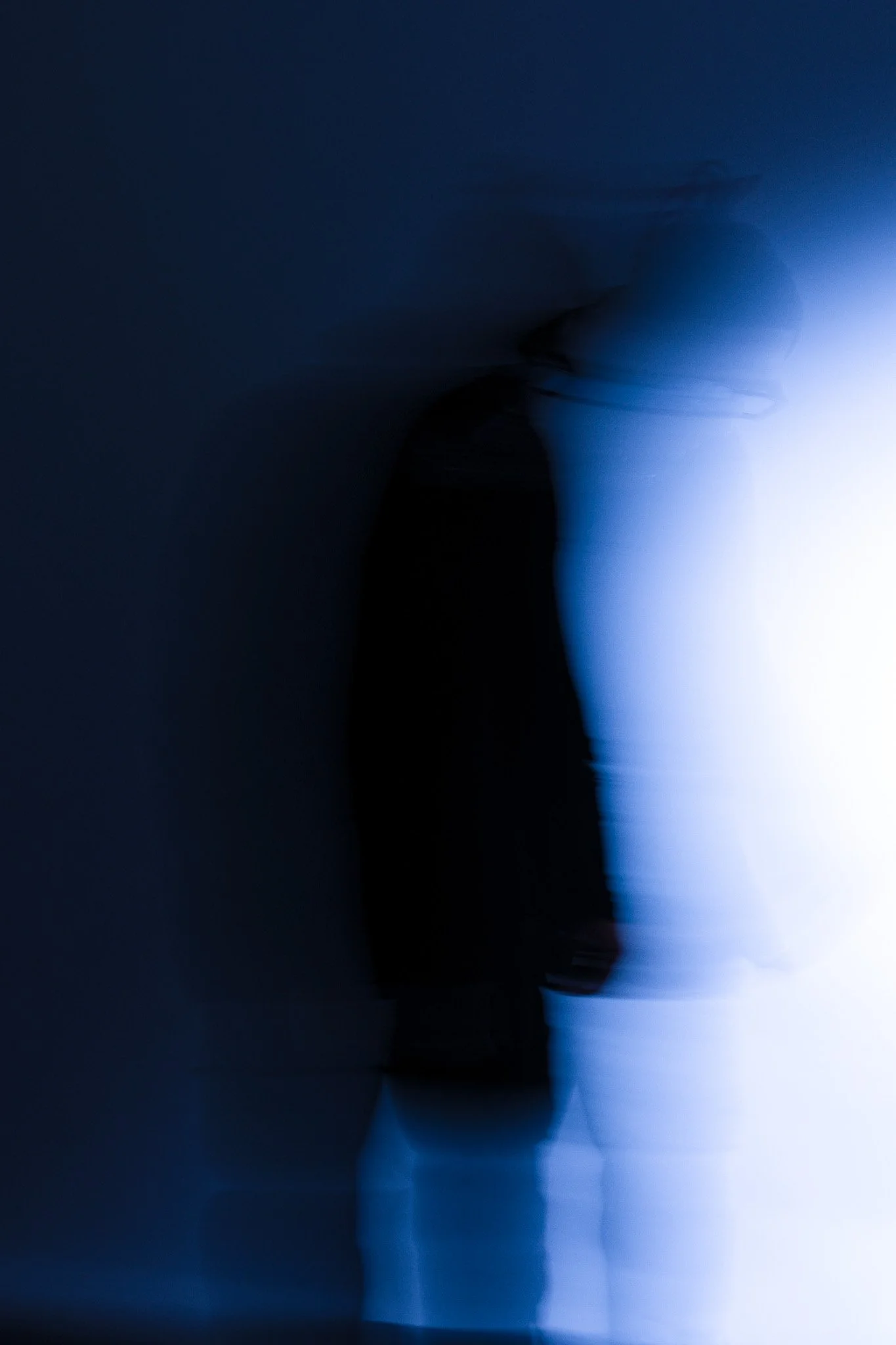 Blurred silhouette of a person standing in front of a bright light, creating a shadowy figure with a soft glow.