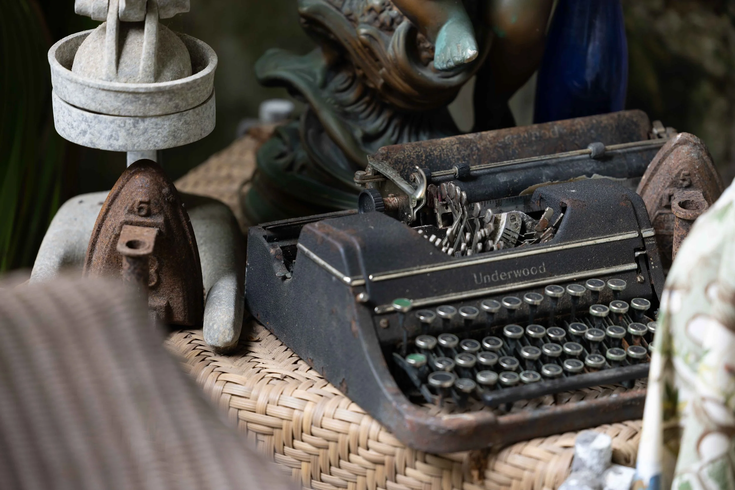 Old Underwood typewriter surrounded by various vintage decorative objects on a woven surface, including ceramic and stone sculptures.