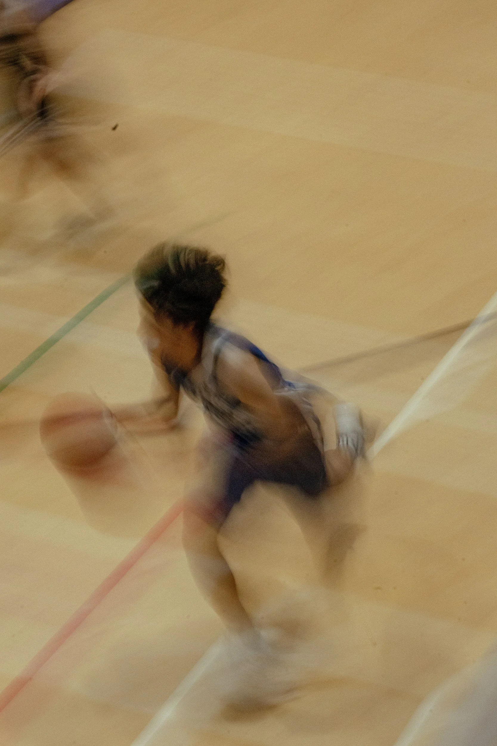 A person is falling or kneeling on a basketball court with a basketball nearby, and another person is partially visible in the top left corner.