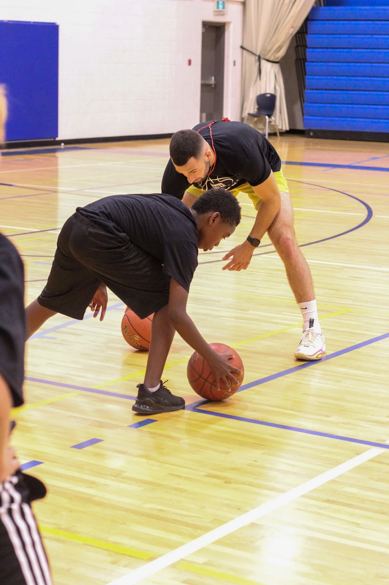 A basketball coach assisting a young player during practice in an indoor gymnasium.