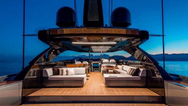 Luxury yacht's outdoor deck with comfortable seating area, surrounded by water and mountains in the background