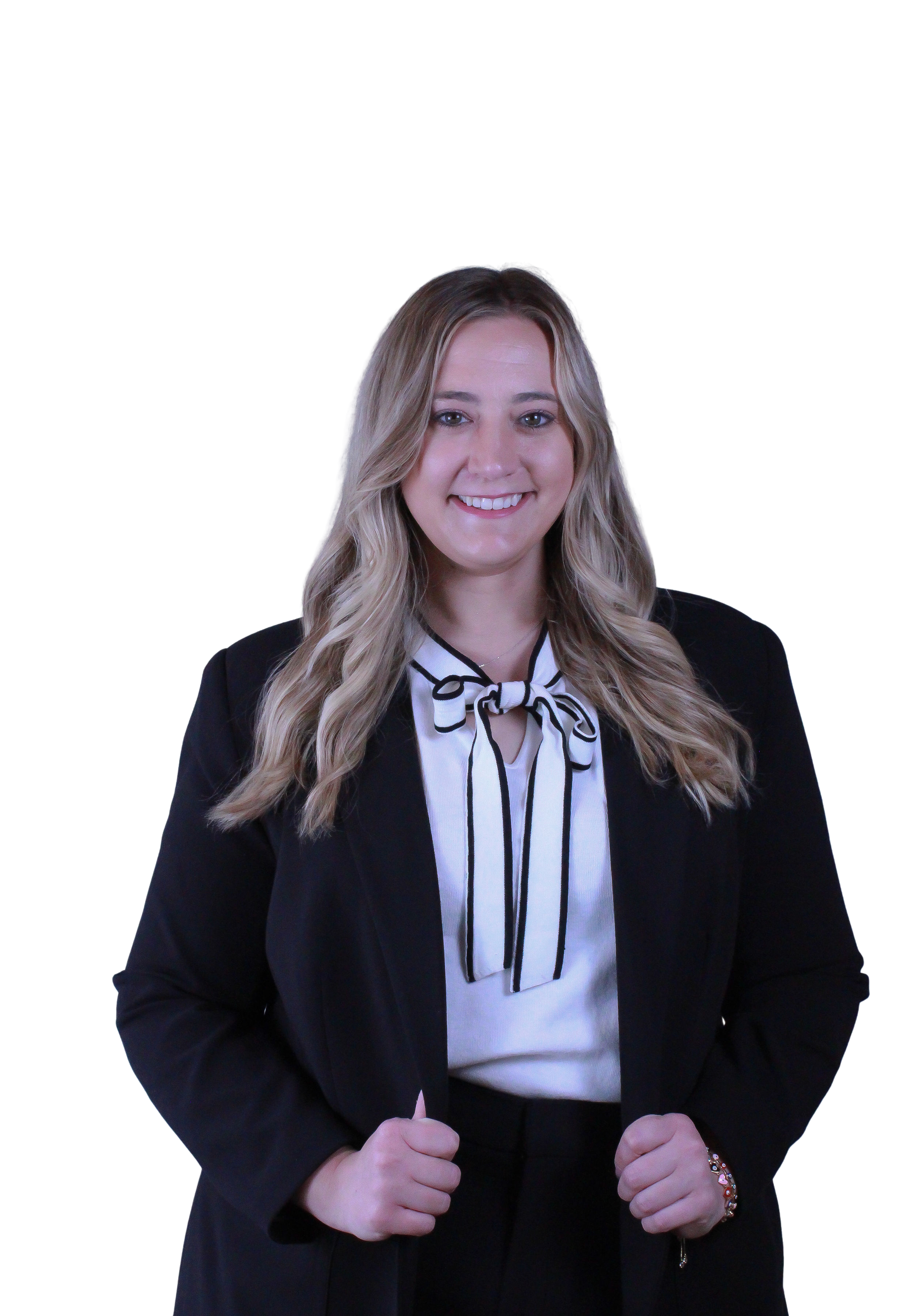 A young woman with long blonde hair smiling and wearing professional black attire with a white blouse and a black and white striped bow tie, standing against a black background.