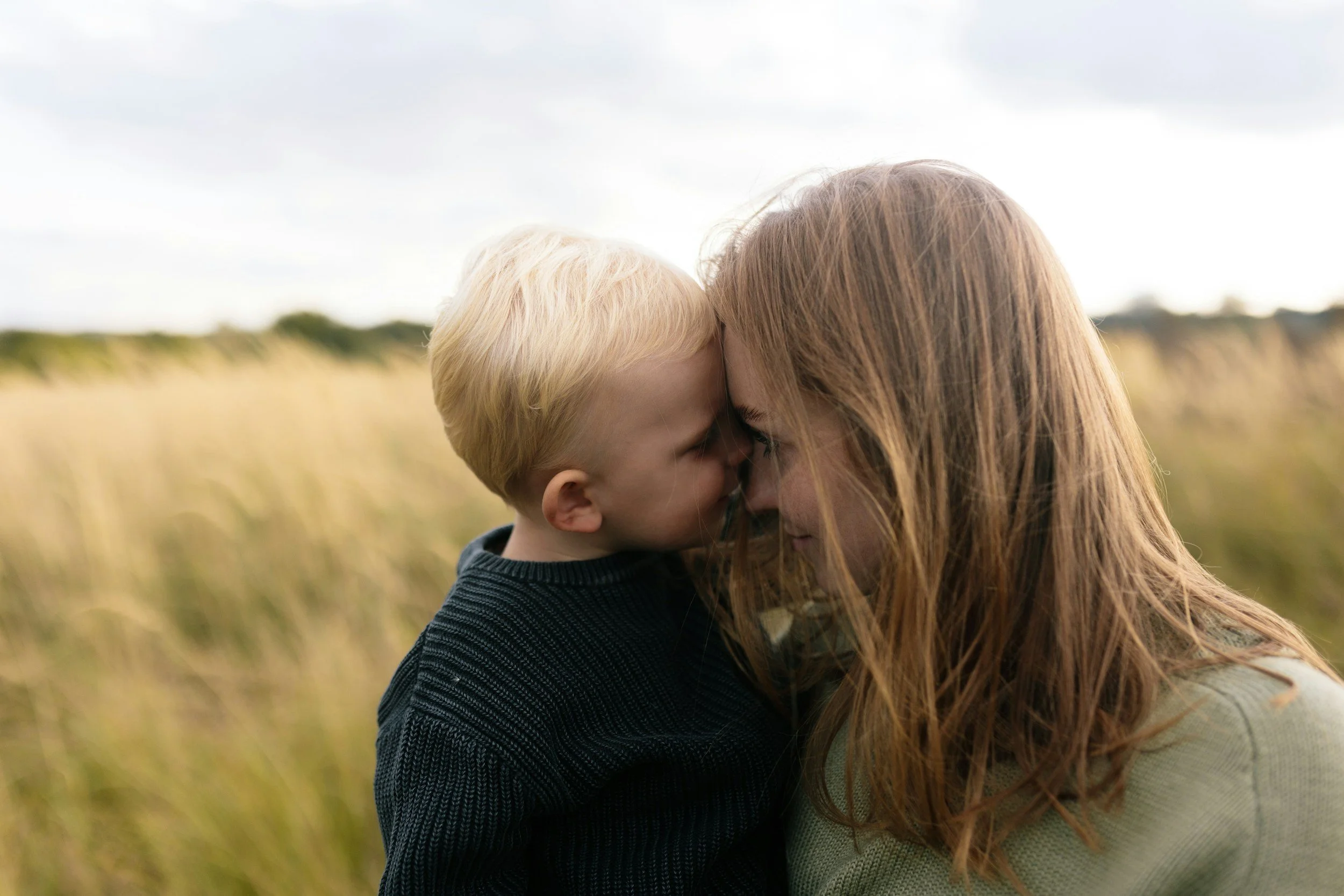 A woman and a young boy sharing a close, affectionate moment outdoors in a field of tall grass.