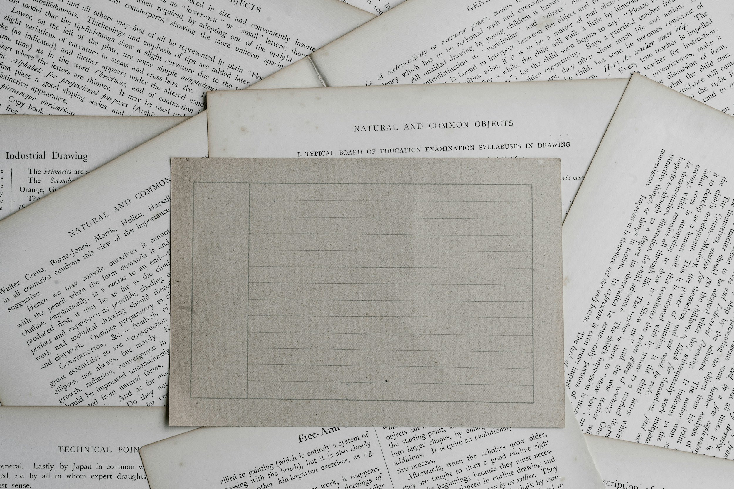 A collection of old, overlapping printed pages with text, some titled 'Natural and Common Objects' and 'Industrial Drawing,' possibly from textbooks or manuals, spread out on a flat surface.
