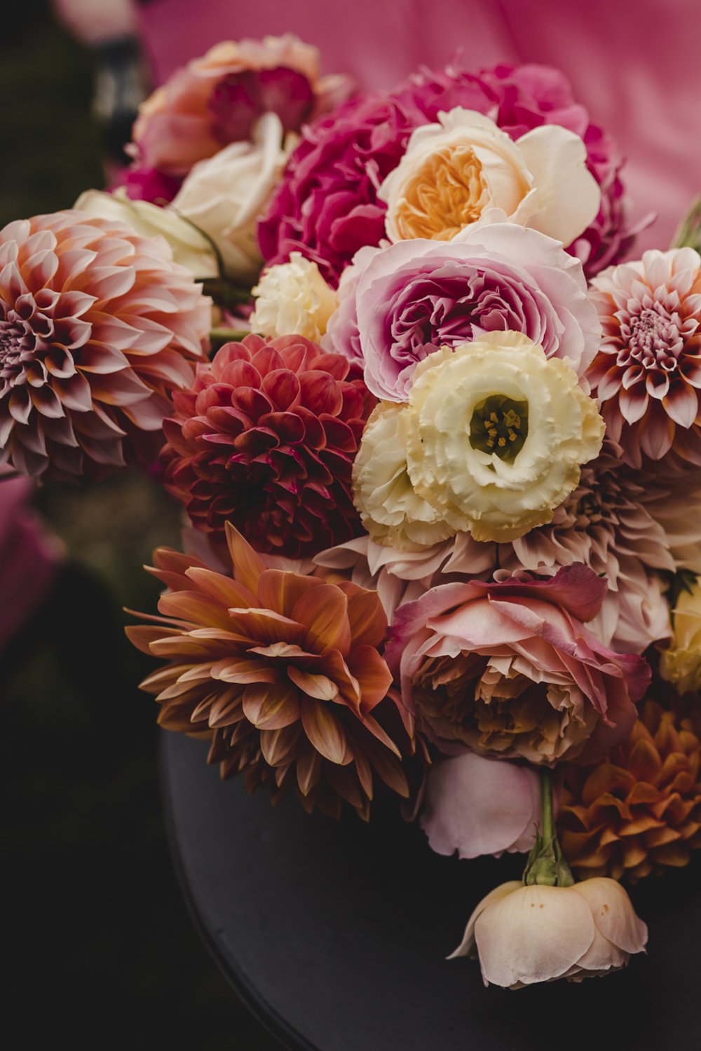 A vibrant wedding bouquet of assorted pink, peach, and white flowers including dahlia, David Austin roses and lisianthus