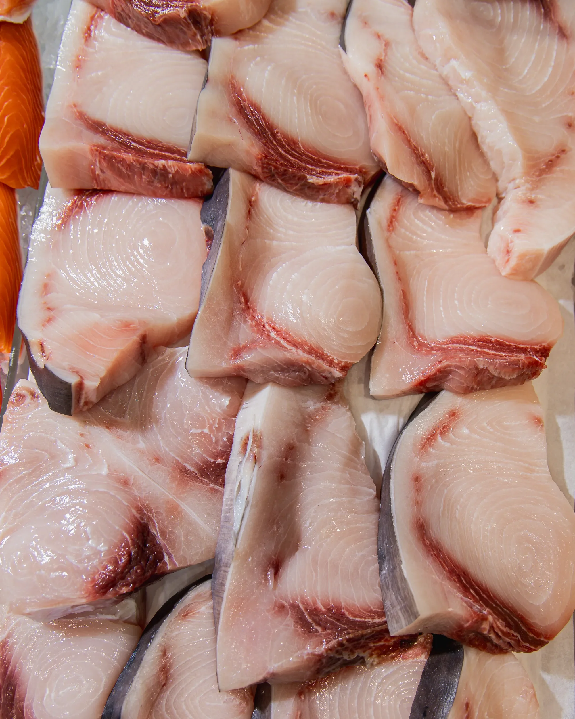 Slices of raw fish with pinkish flesh and dark skin, laid out on a surface.
