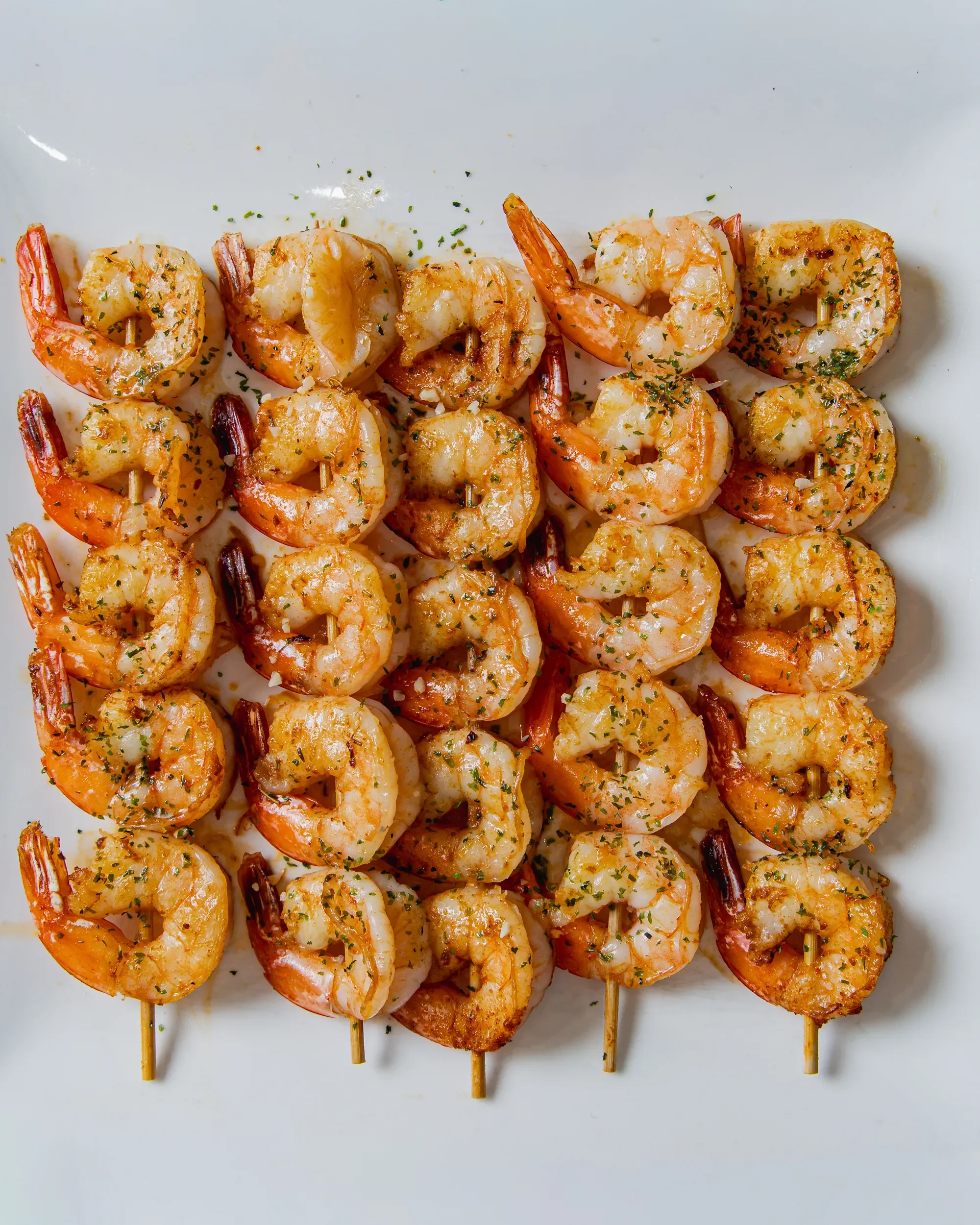 Skewers of grilled shrimp garnished with herbs on white surface.