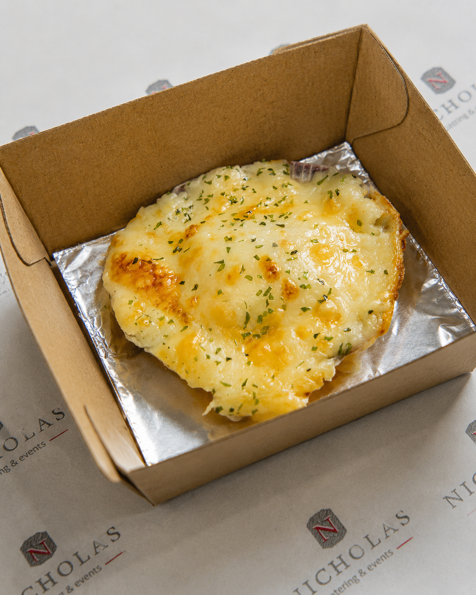 Cheeseless pizza with melted cheese and herbs in a cardboard takeout box and foil lining.