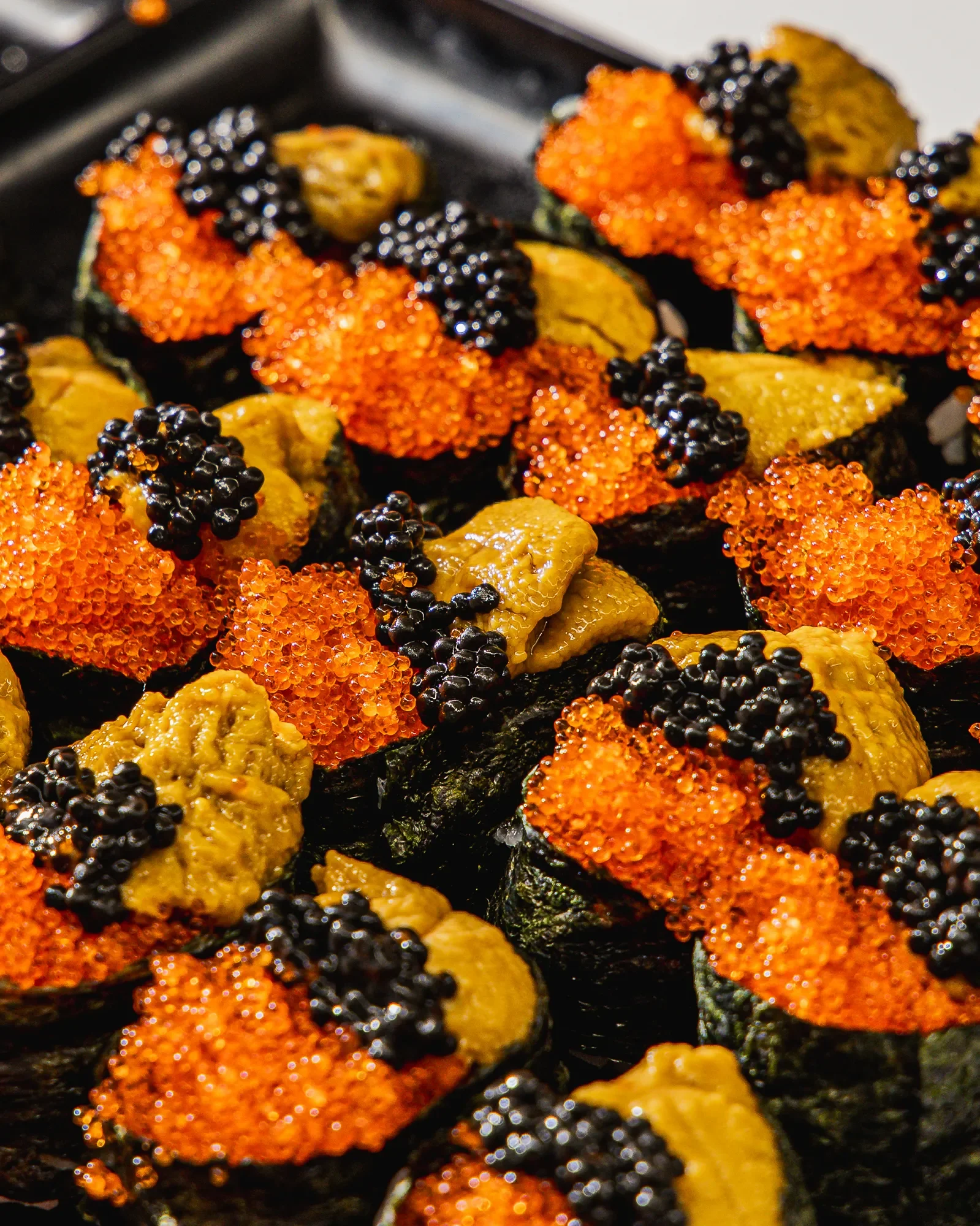 Close-up of sushi rolls topped with orange fish roe and black caviar.