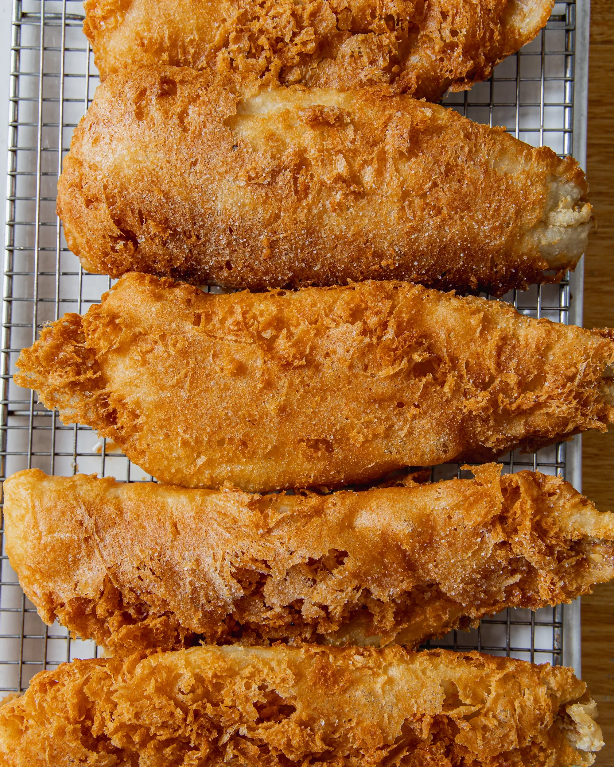 Close-up of several pieces of fried fish fillets with golden, crispy breading on a metal cooling rack.
