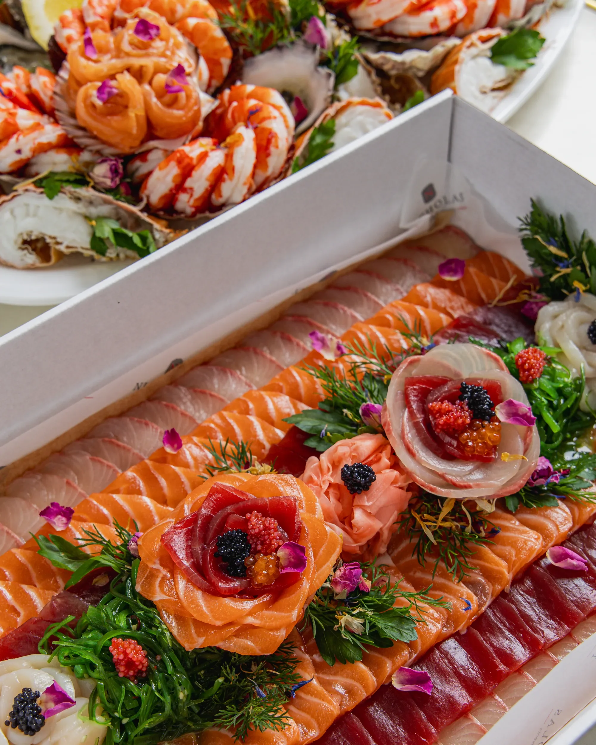A platter of assorted sashimi, including salmon, tuna, and other fish, garnished with herbs, flowers, and roe.