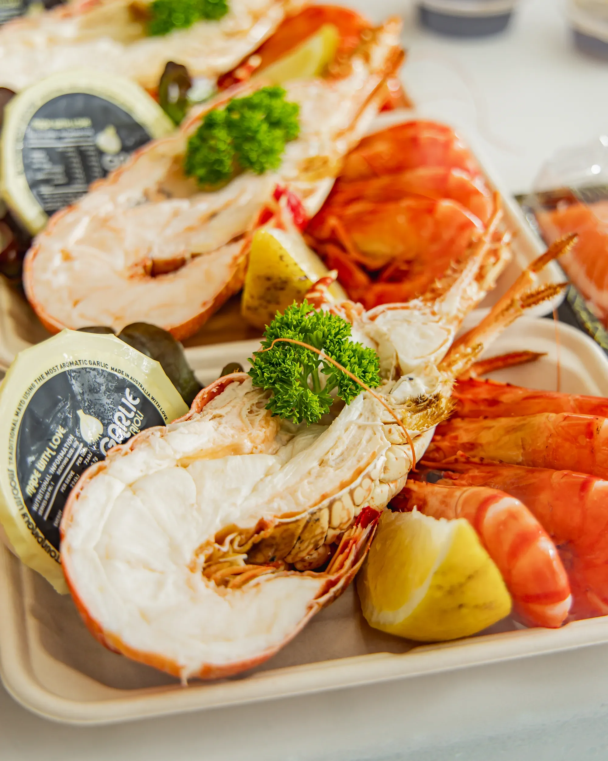Close-up of a seafood platter with lobster tails garnished with parsley, lemon wedges, and other seafood items in the background.