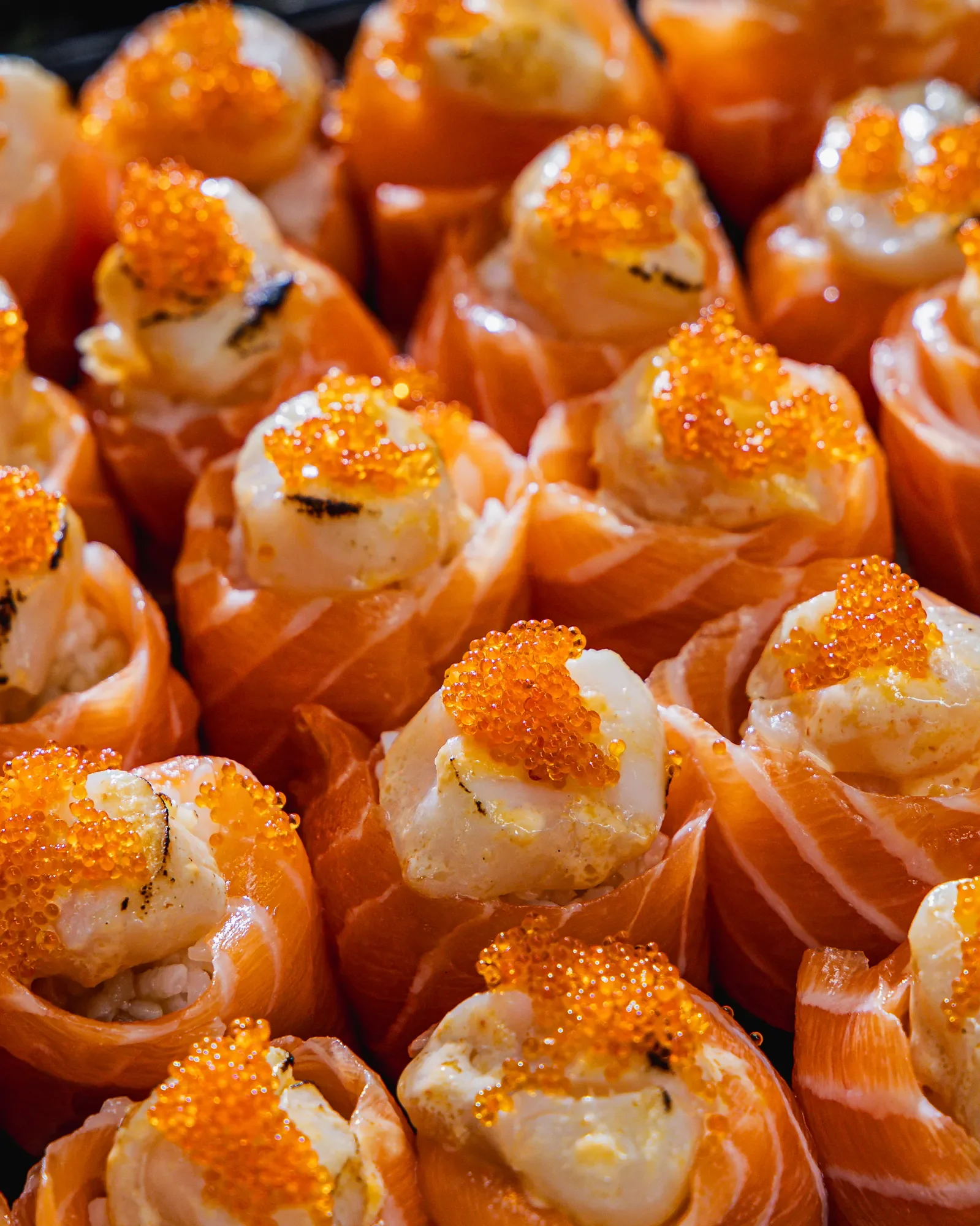 Close-up of salmon sushi rolls topped with orange fish roe and creamy topping.