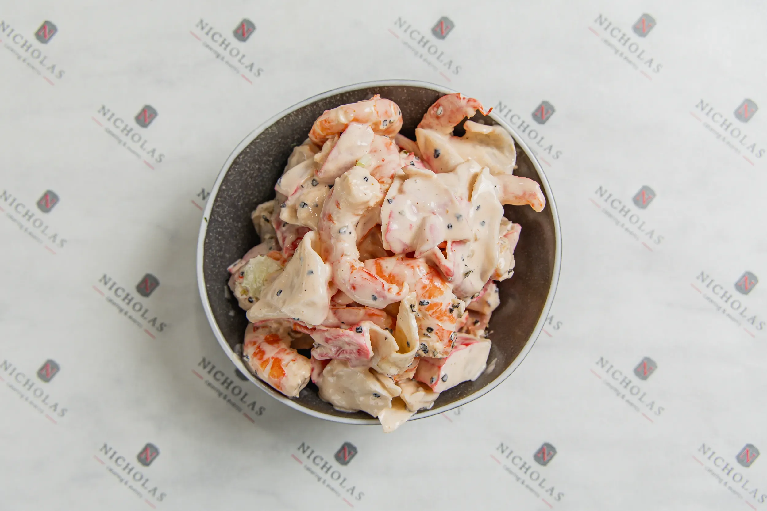 A bowl of potato salad with mayonnaise, carrots, black pepper, and other ingredients on branded paper.