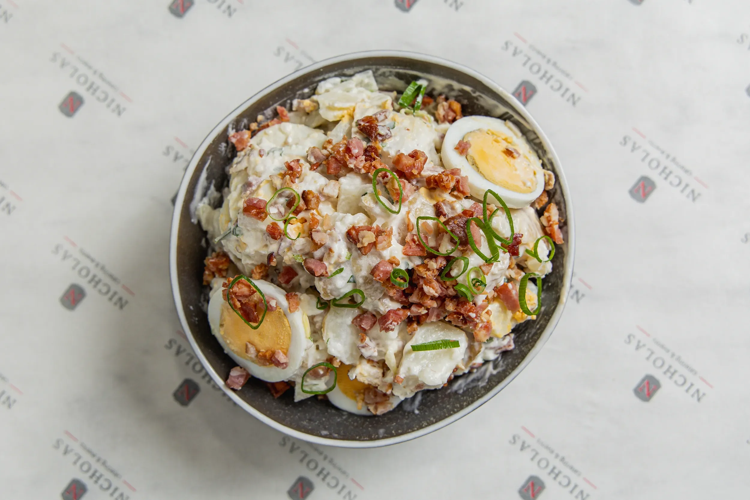 Salad with sliced eggs, chopped bacon, green onions, and creamy dressing, served in a bowl on branded paper.