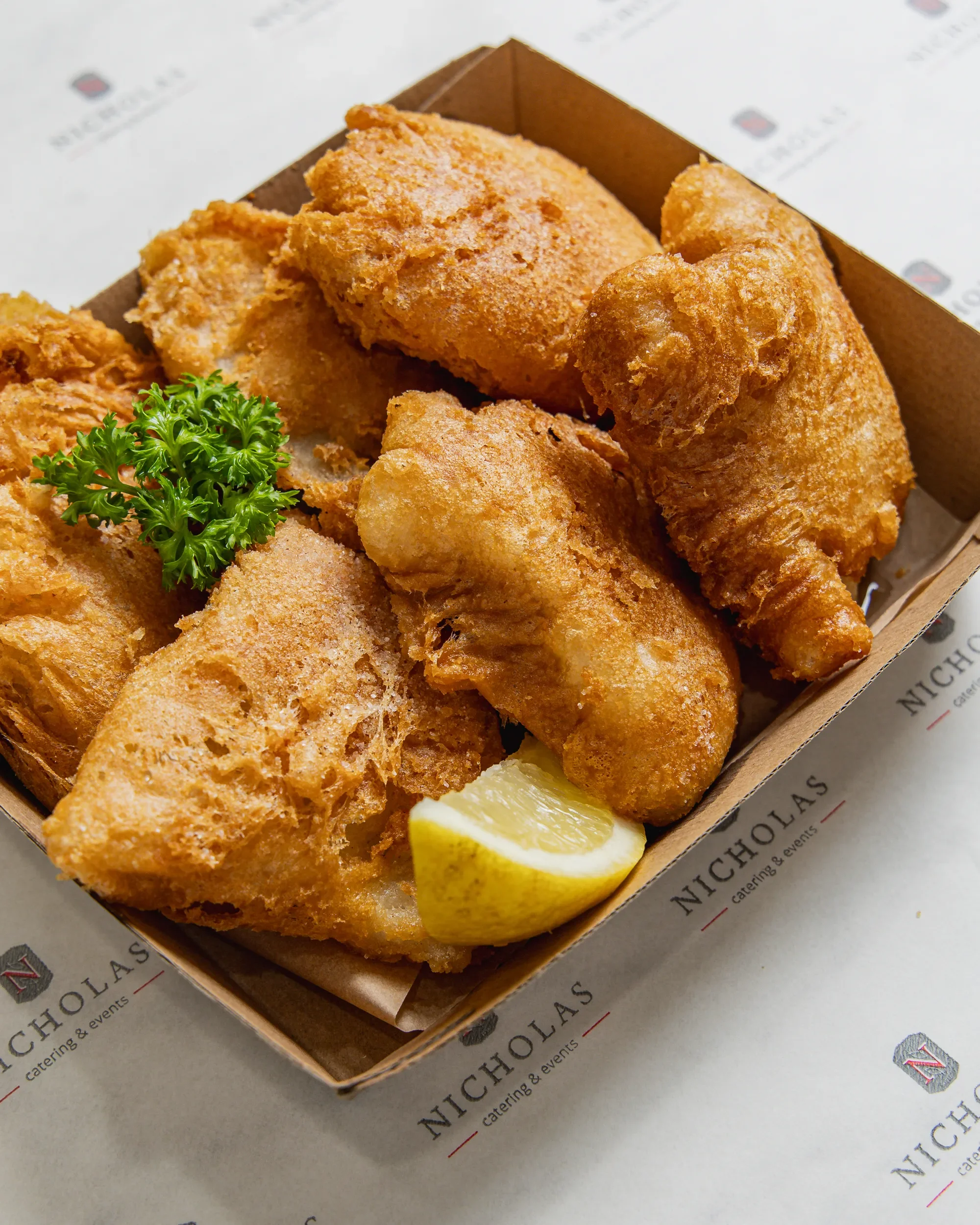 Fried chicken tenders with a lemon wedge and parsley on a paper-lined tray, with a restaurant branding visible.