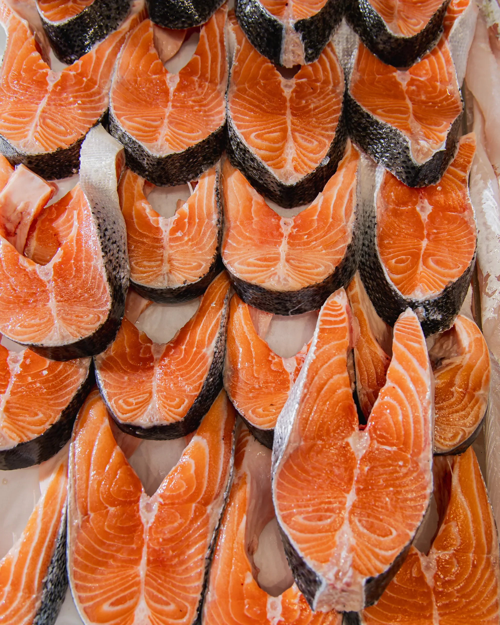 Close-up of raw salmon fillets with orange flesh and black skin.